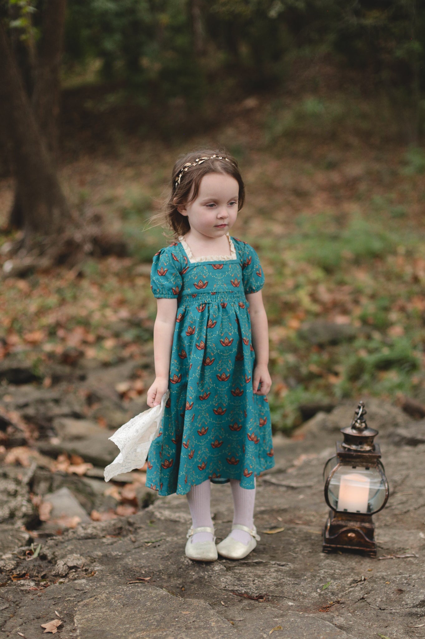 Young girl wearing modest dress with lantern outdoors.