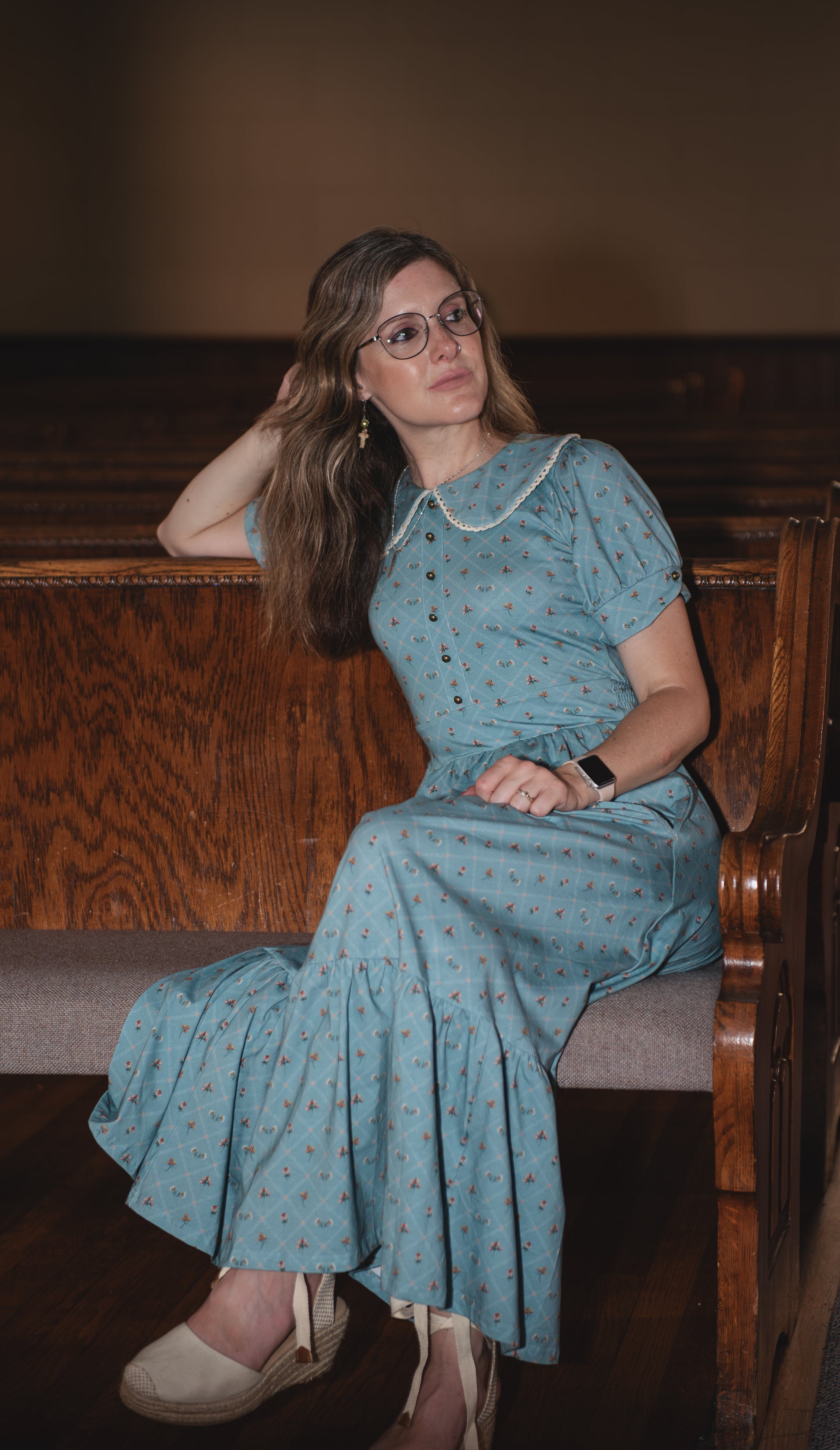 Woman in a blue modest nursing dress sitting on a wooden bench indoors