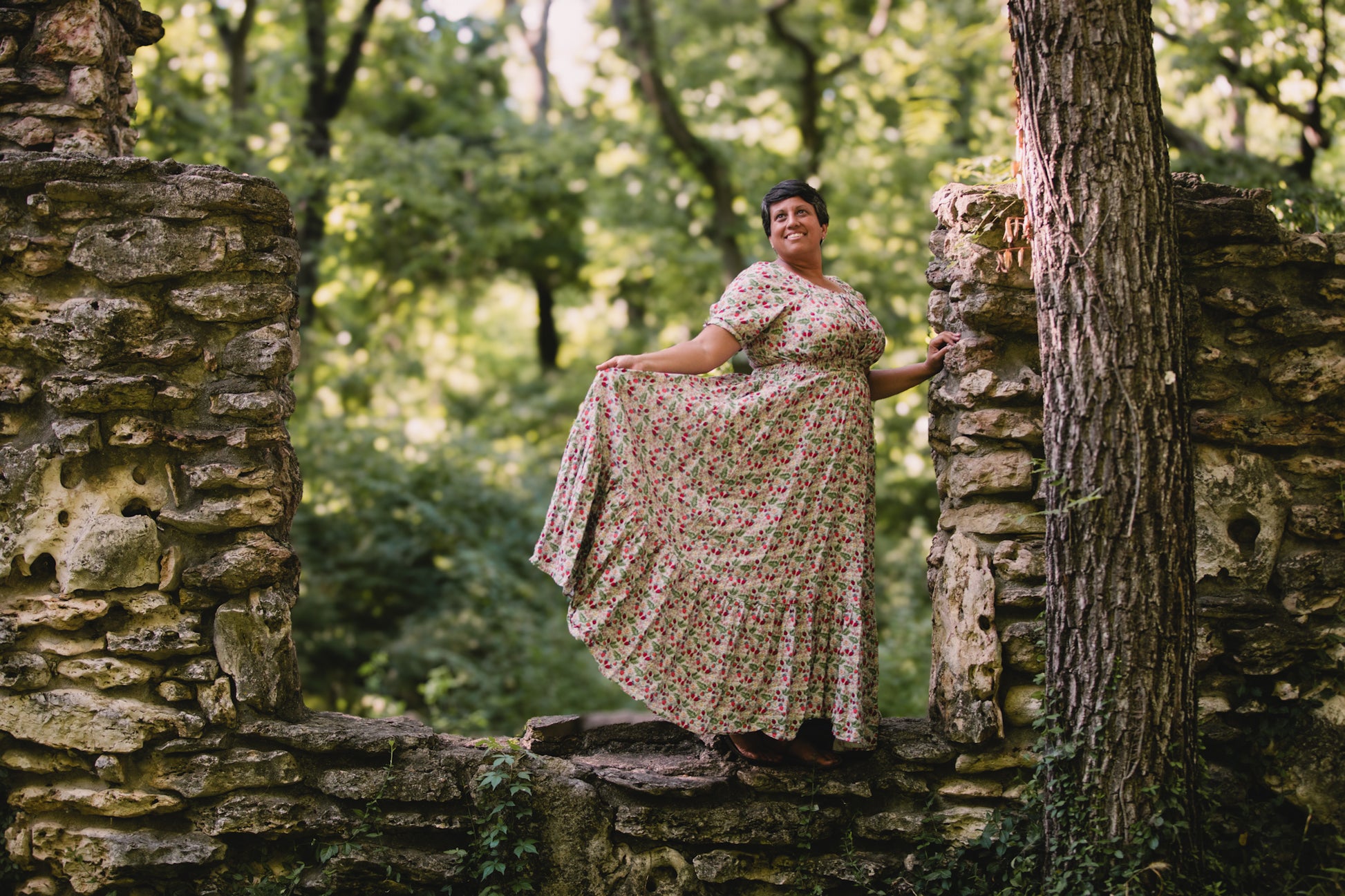 Woman in a floral modest nursing dress standing among stone ruins and trees