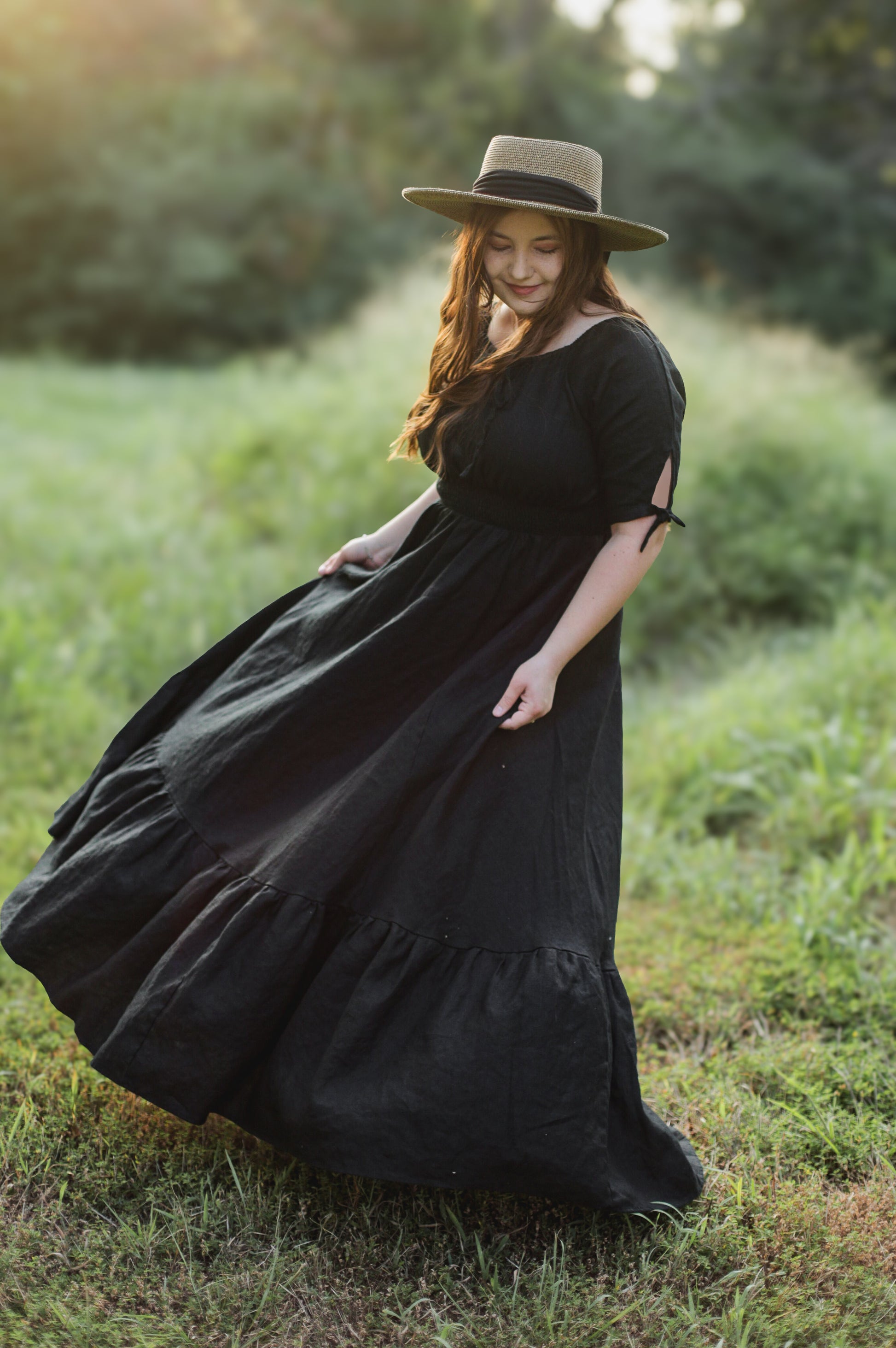 Woman in a black modest nursing dress and hat standing in a grassy field