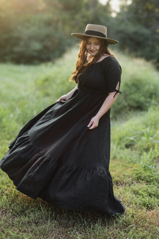 Woman in a black modest nursing dress and hat standing in a grassy field