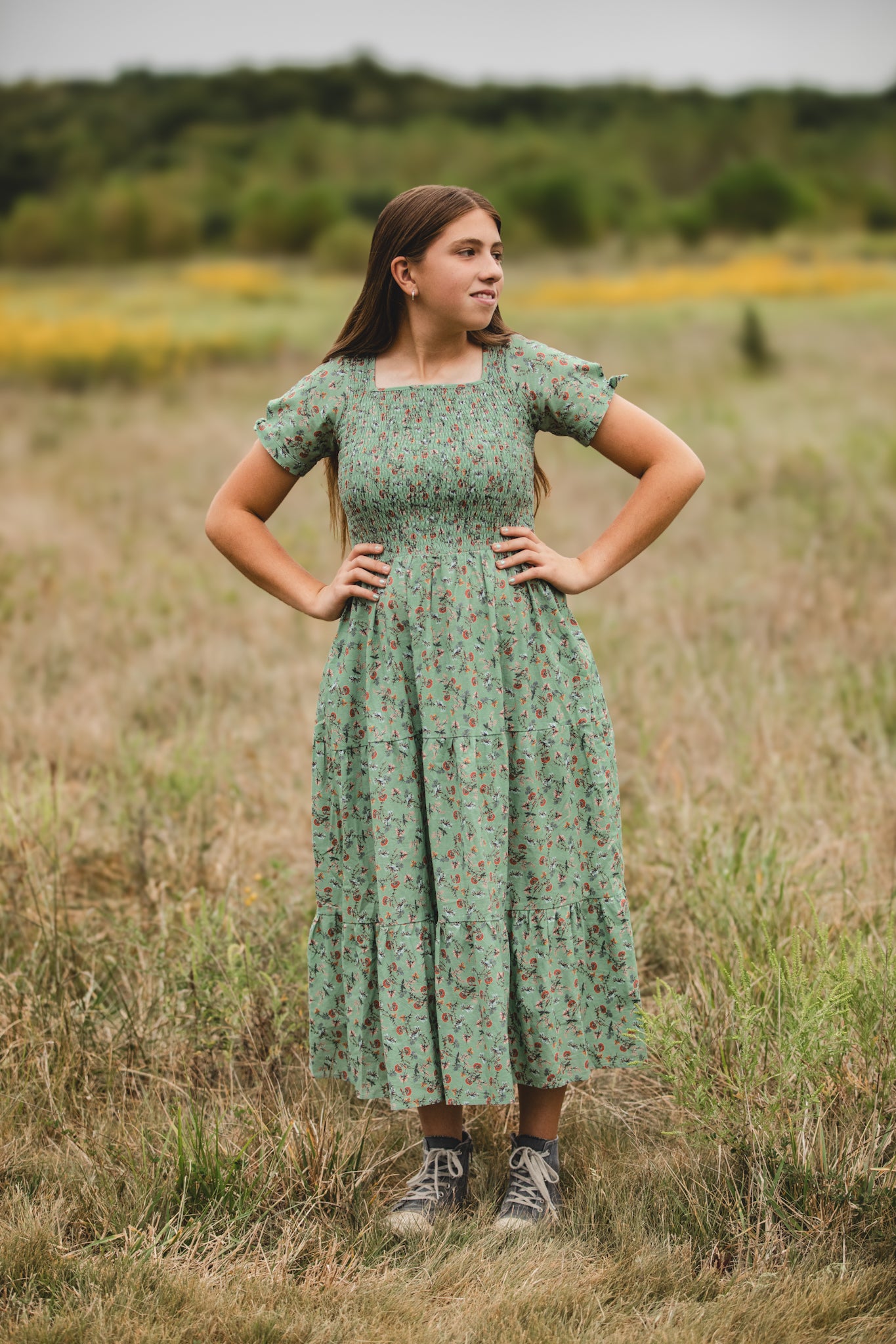 Woman in a floral dress standing in a field with hands on hips