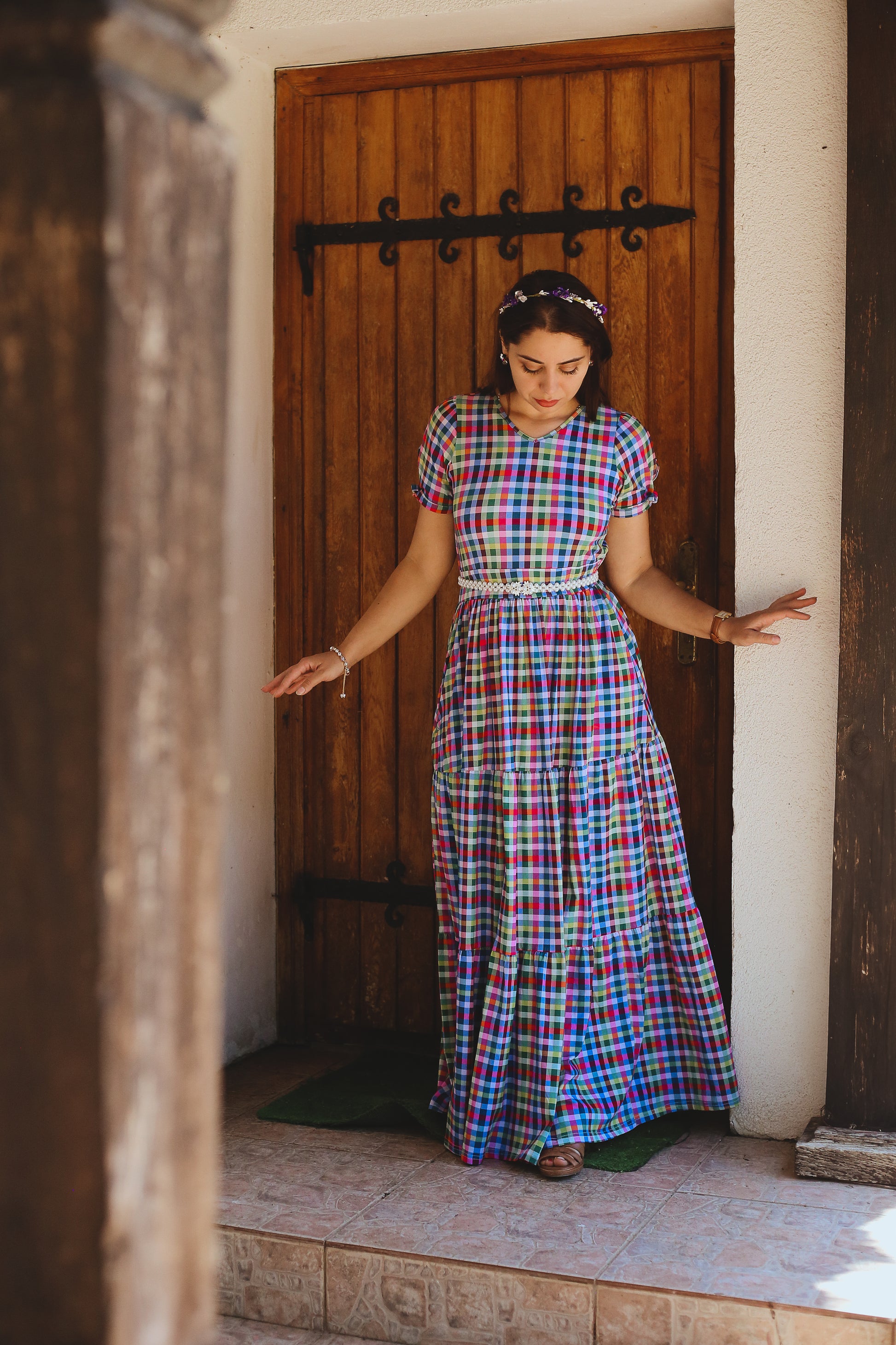 Woman in a colorful plaid modest nursing dress standing in front of a wooden door.