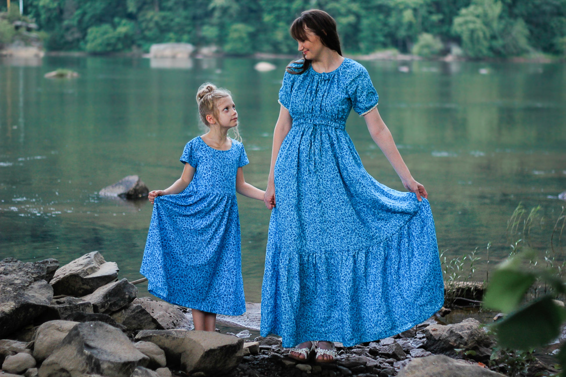 Woman and young girl in matching blue modest dresses standing by a lake.