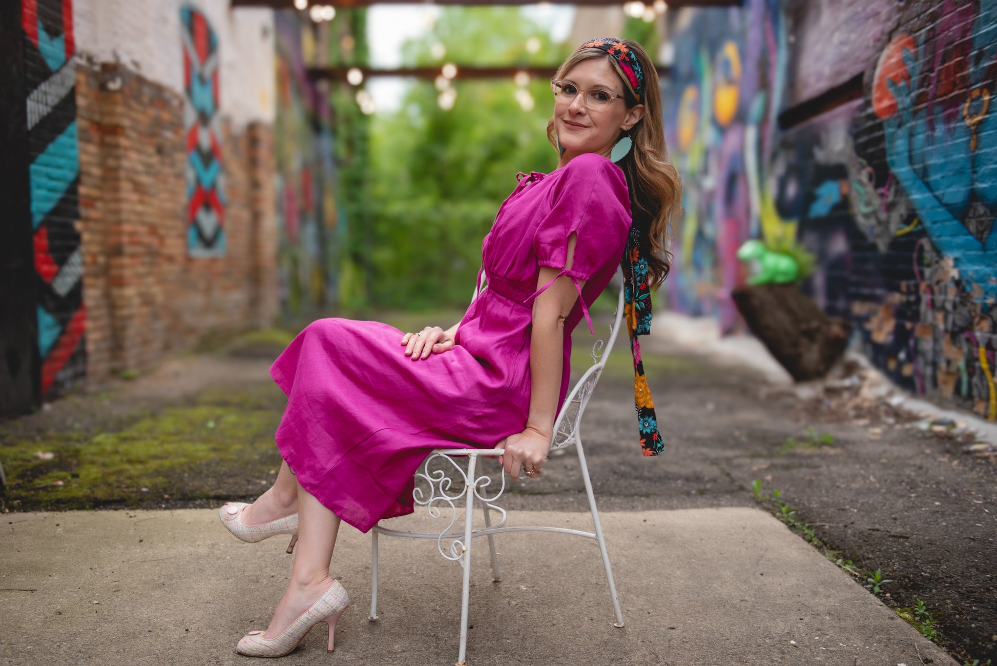 Woman in a pink modest nursing dress sitting on a chair against a graffiti-covered wall.