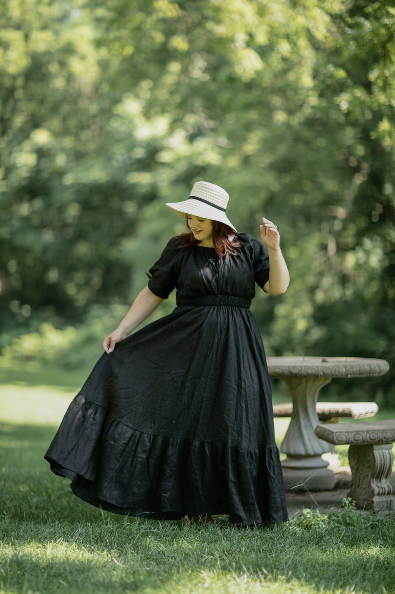 Woman in a black modest nursing dress and hat standing in a park