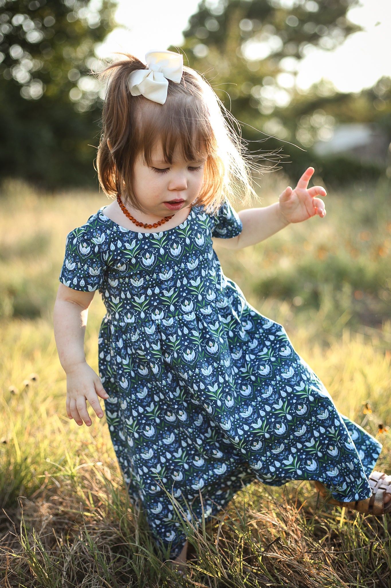 Child in blue floral dress standing in grassy field
