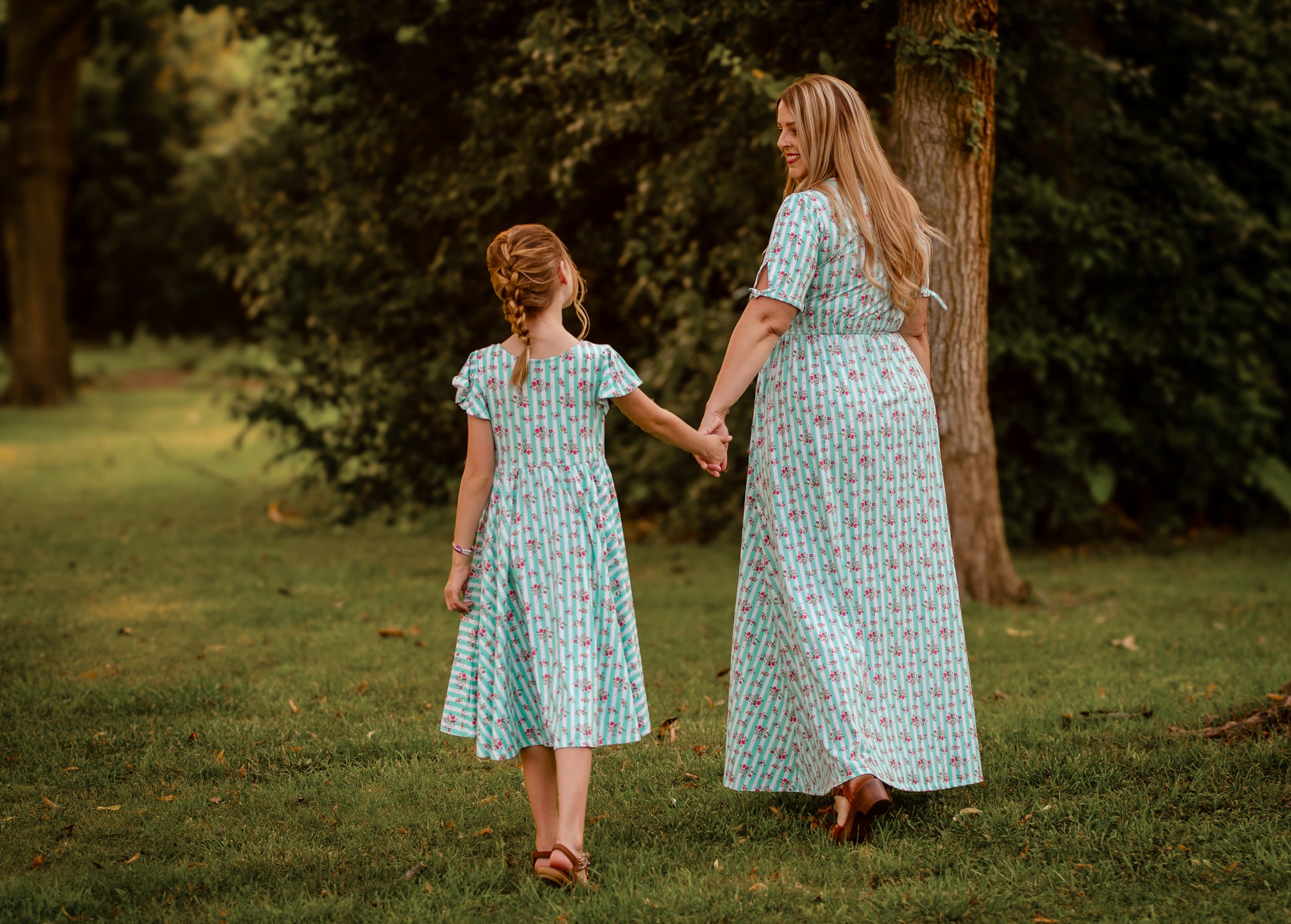 Woman and young girl holding hands in a park wearing modest dresses.