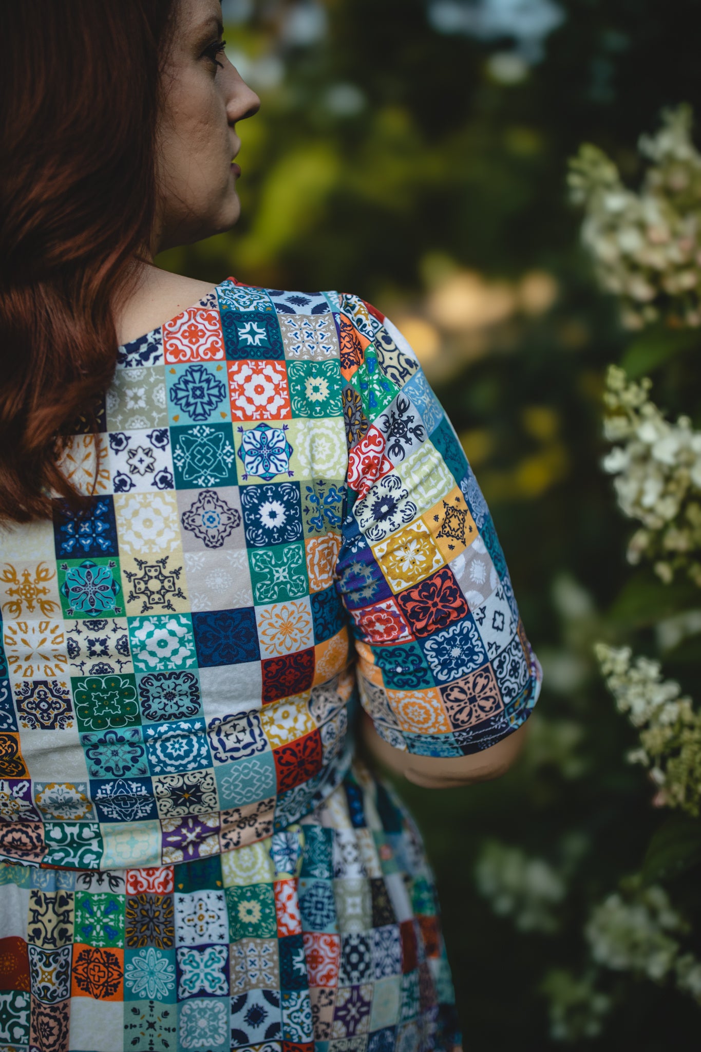 Woman wearing a colorful patchwork modest nursing dress standing outdoors with greenery in the background