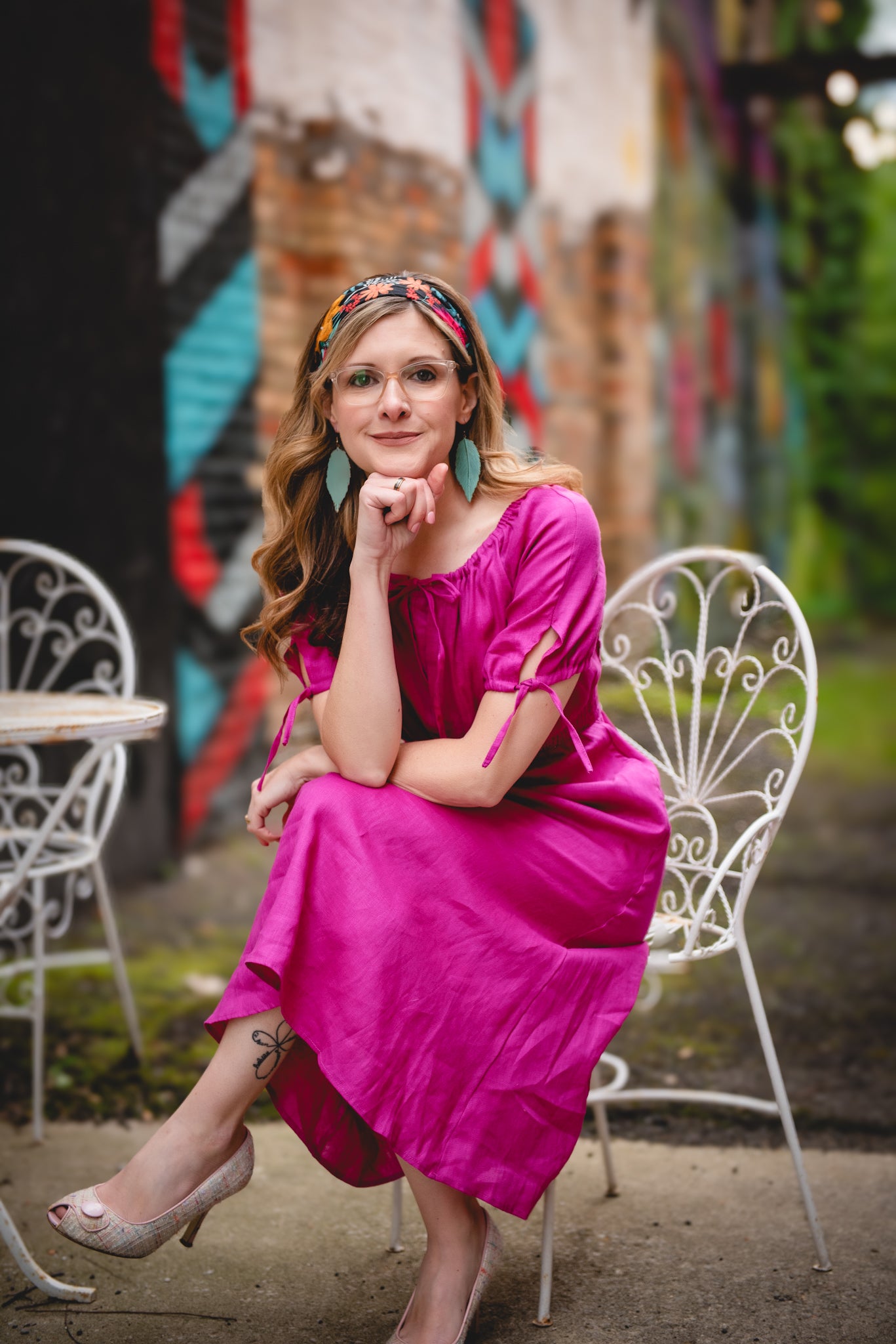 Woman in a pink modest nursing dress sitting on a chair with a colorful mural in the background