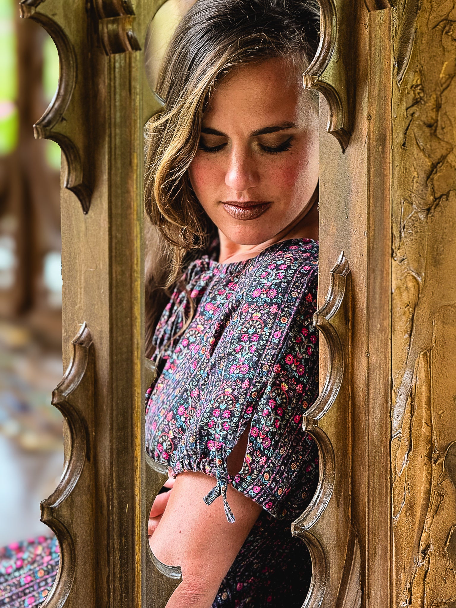 Woman in a floral modest nursing dress standing behind an ornate wooden door.