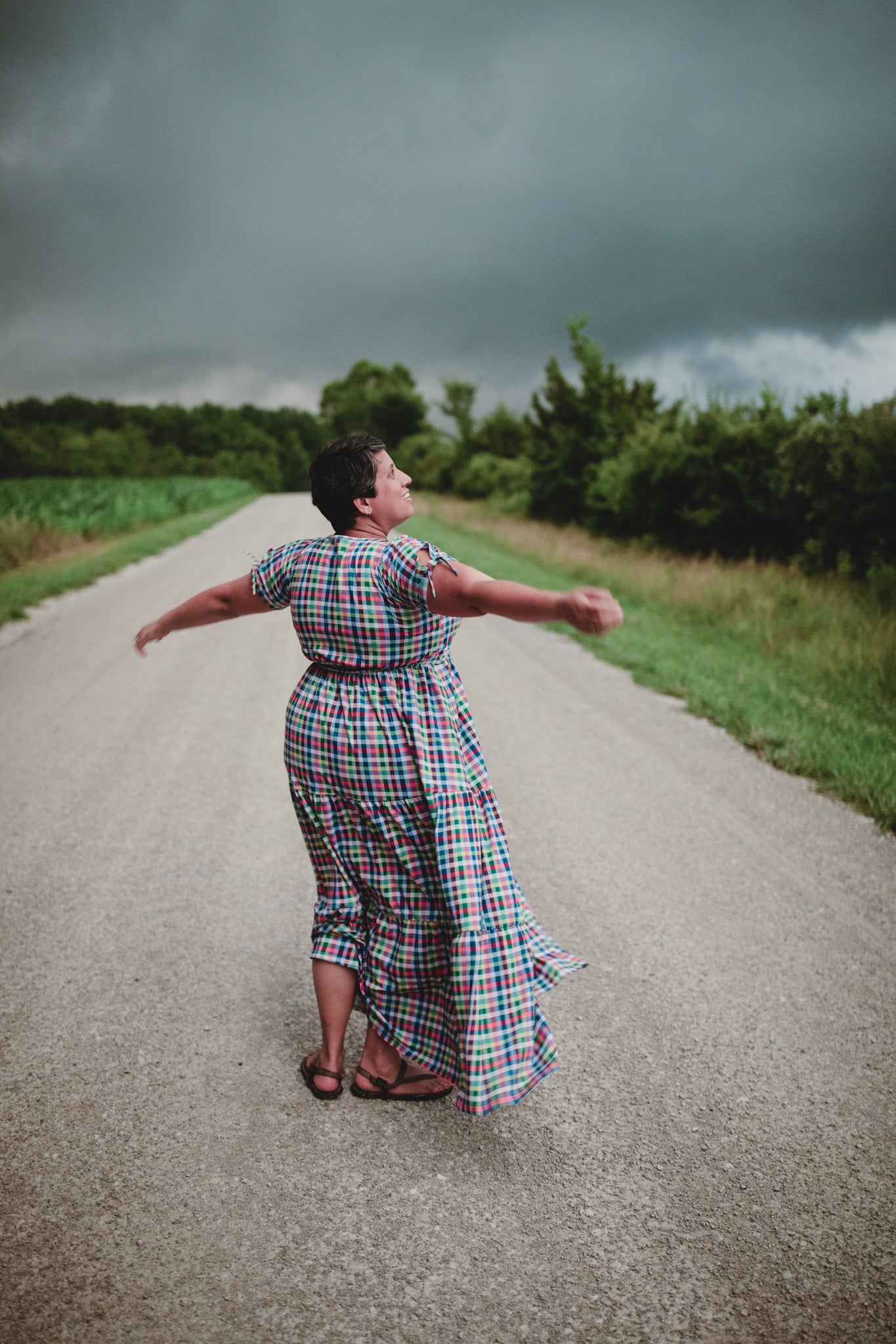 Person in a plaid modest nursing dress standing on a road with arms outstretched, under a dark sky.