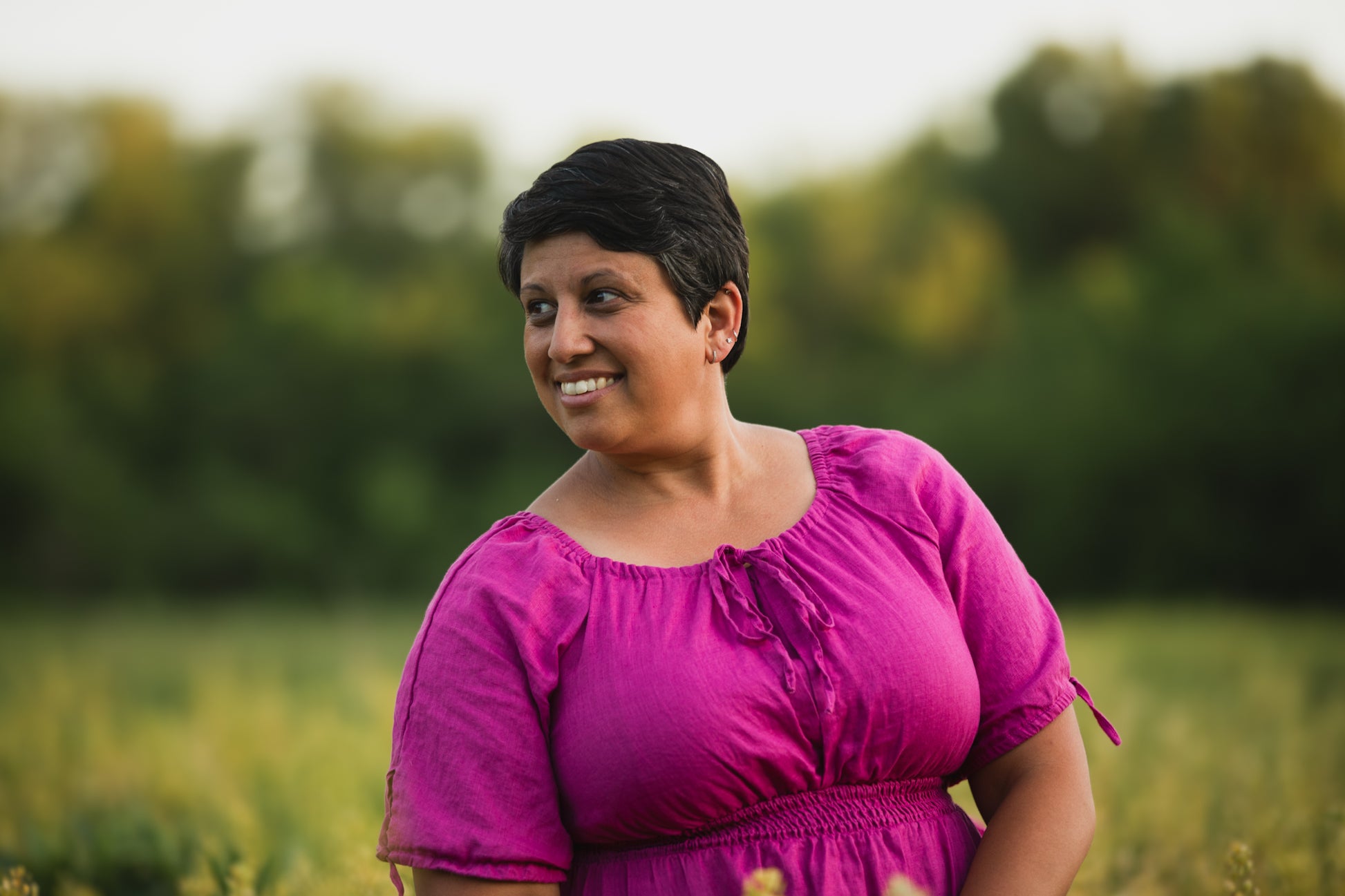 Woman in a pink modest nursing dress standing in a field with trees in the background