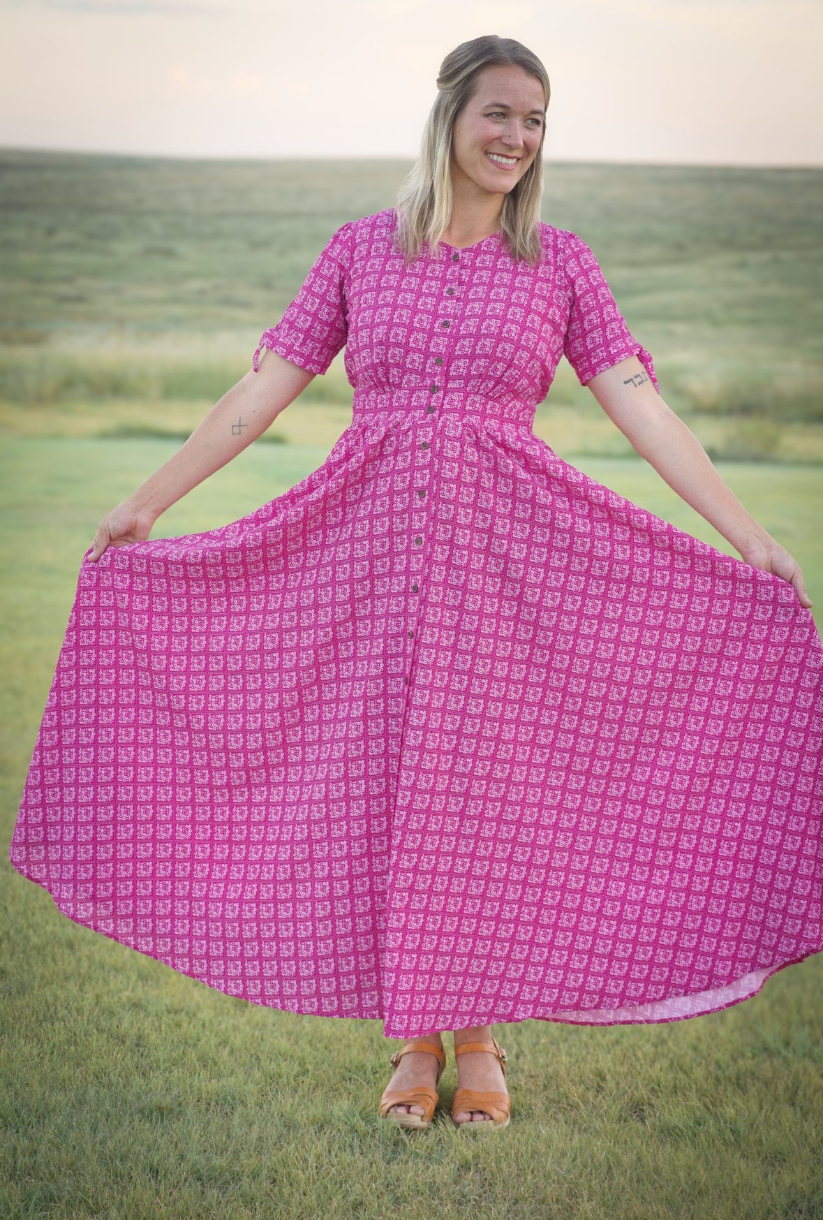 Woman in a pink modest nursing dress standing in a field with a scenic background