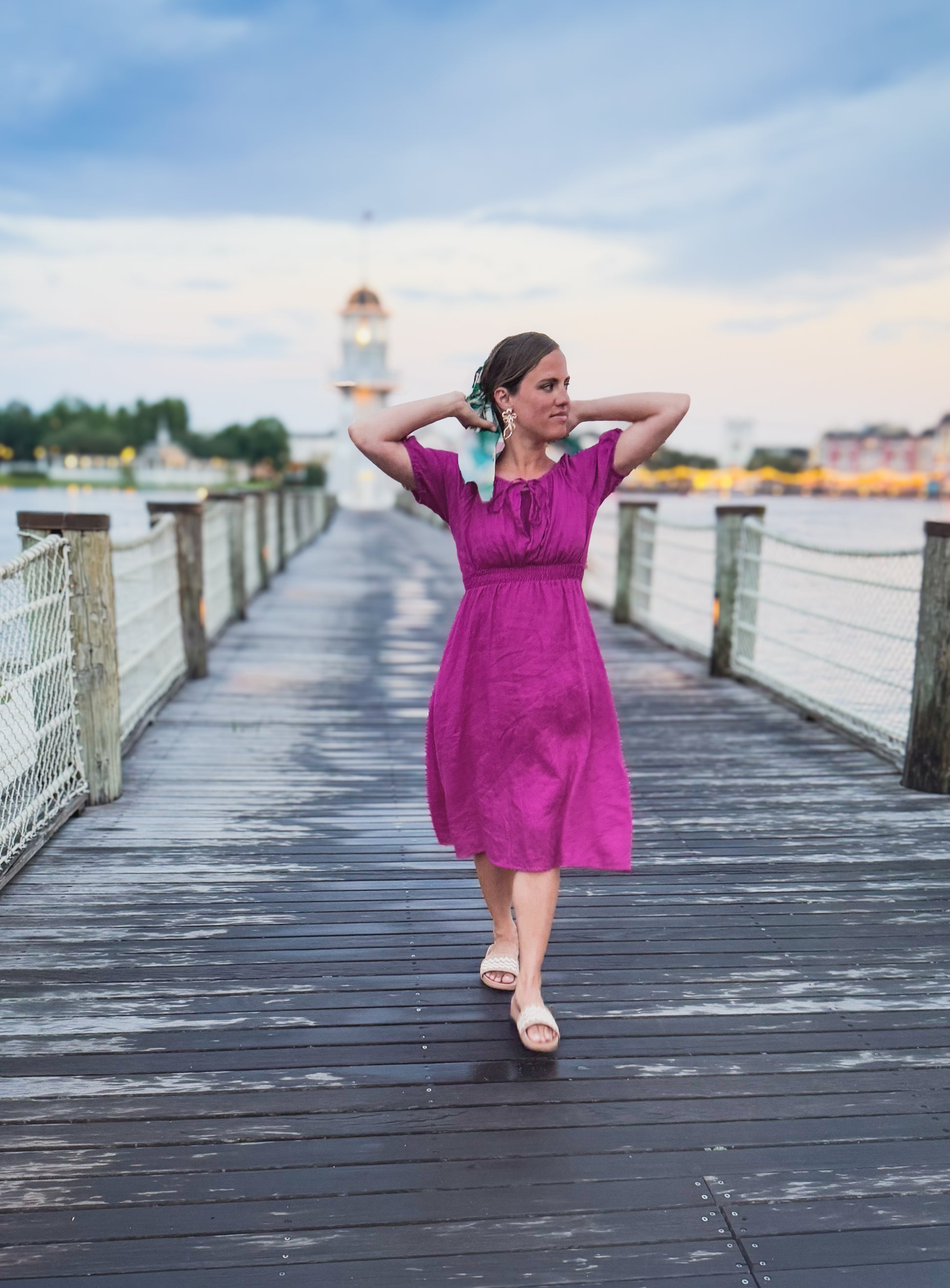 Woman in a pink modest nursing dress walking on a wooden pier with a scenic background