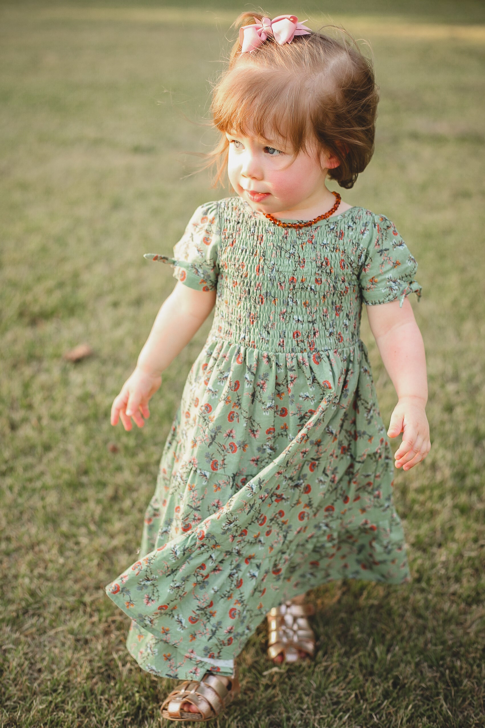 Young girl in a green floral dress standing on grass