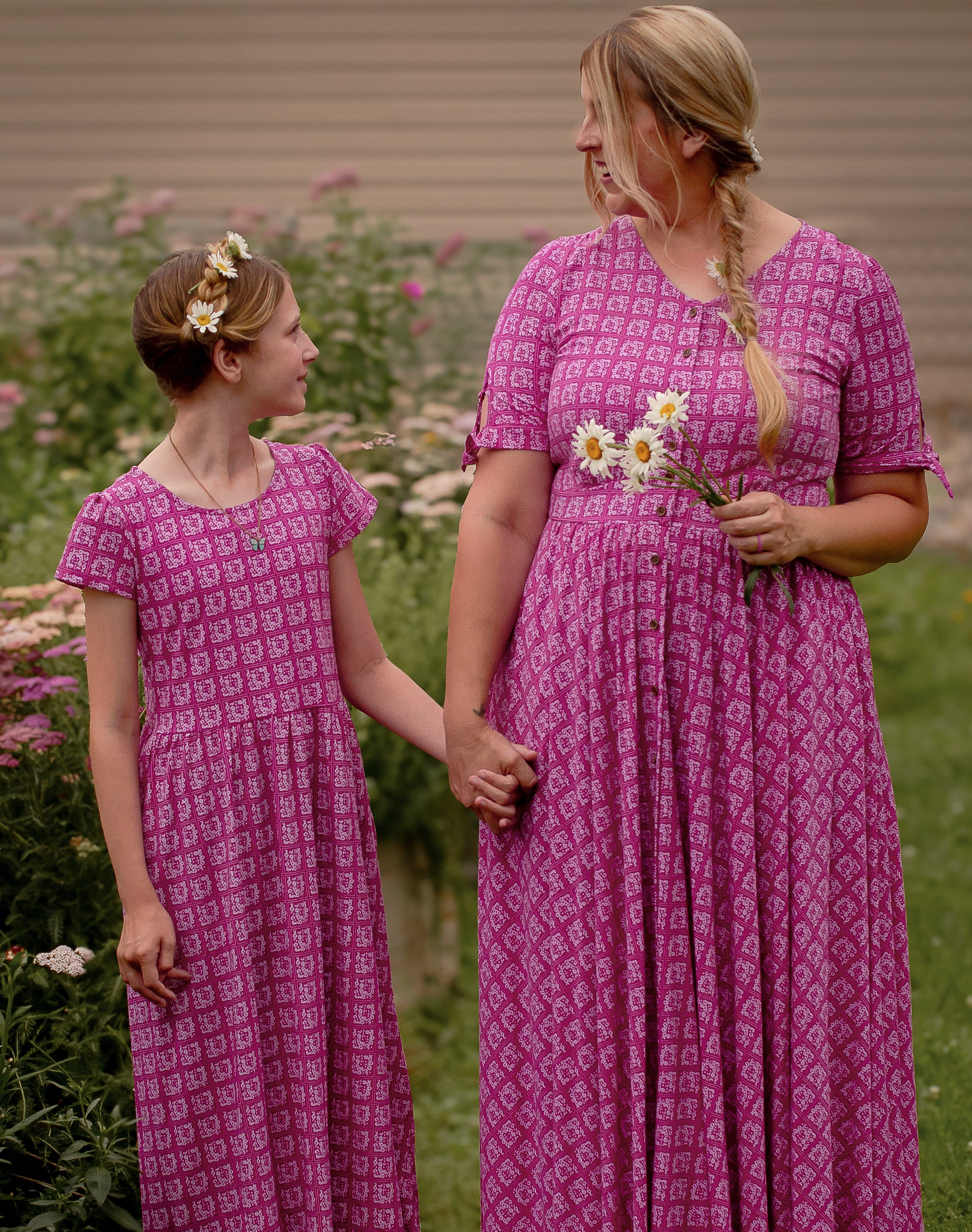 Mother and daughter in matching pink modest dresses standing outdoors with flowers.