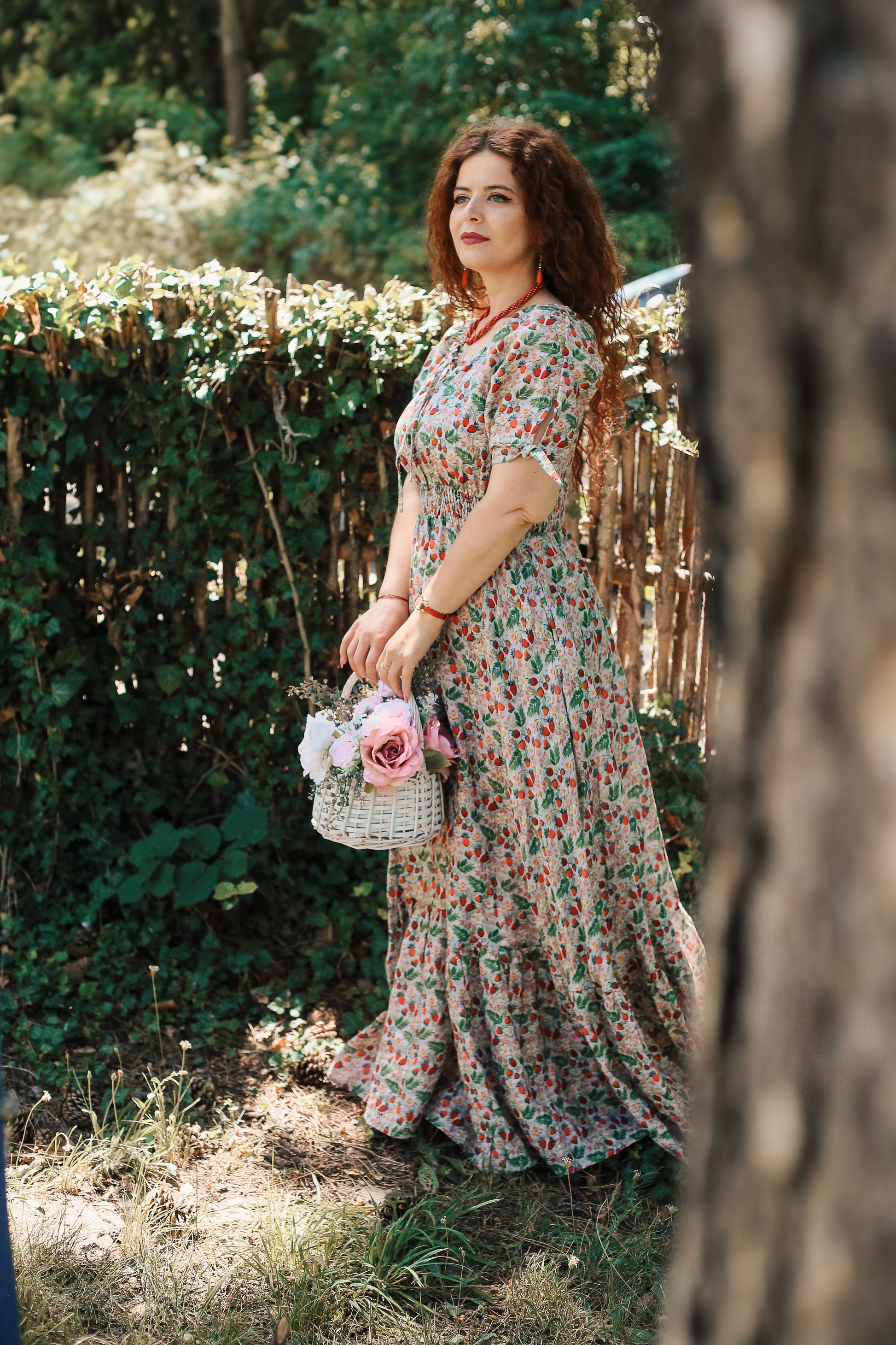 Woman in a floral modest nursing dress holding a small bouquet of flowers, standing in a garden.