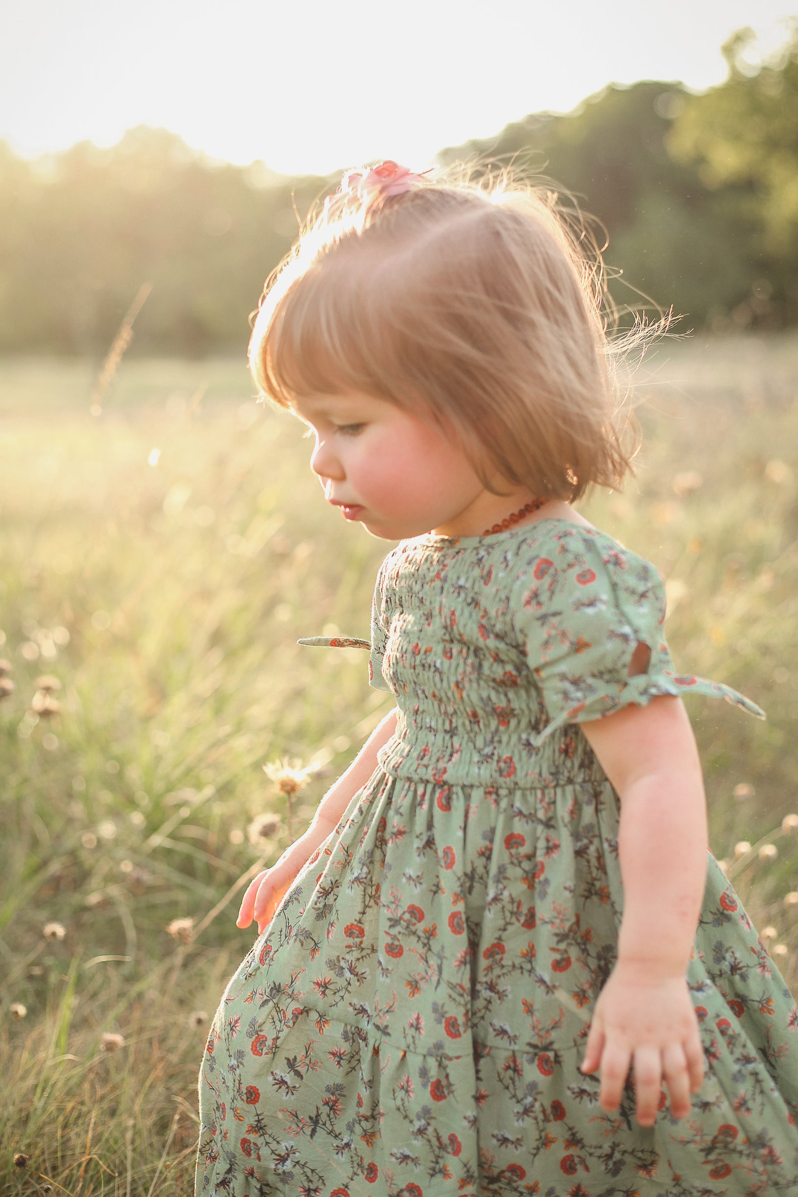 Child in a floral dress standing in a sunlit field