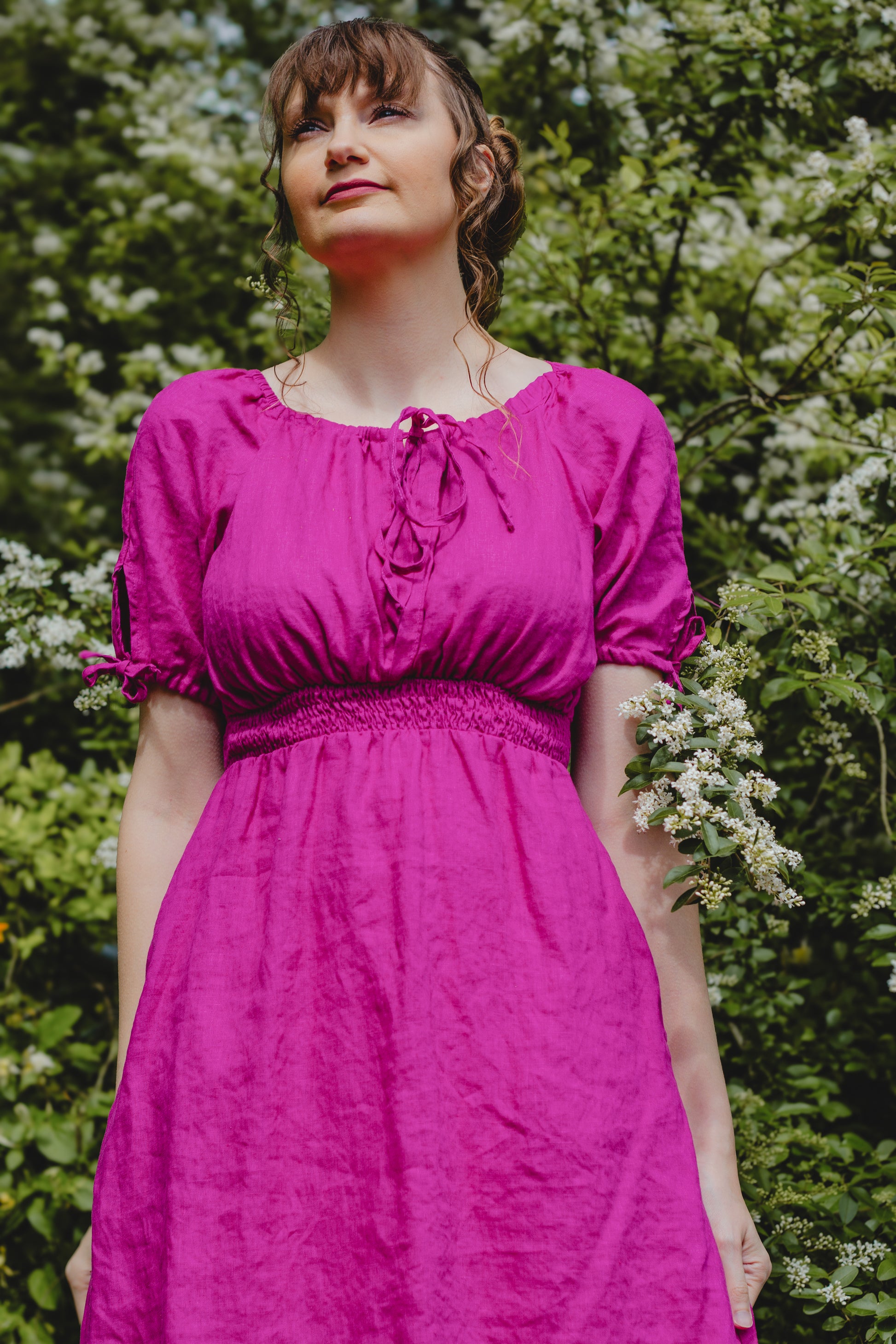 Woman wearing a pink modest nursing dress standing in front of green foliage