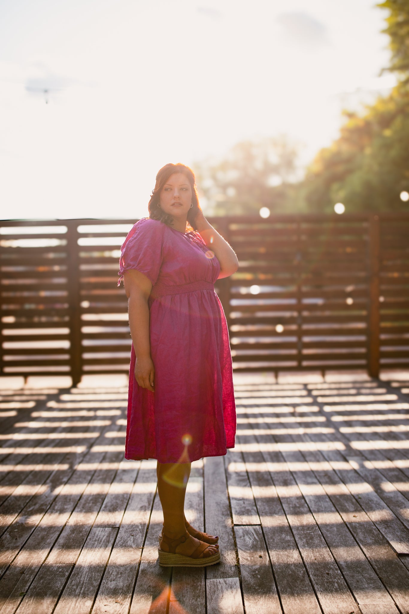 Woman in a pink modest nursing dress standing on a wooden deck with trees in the background