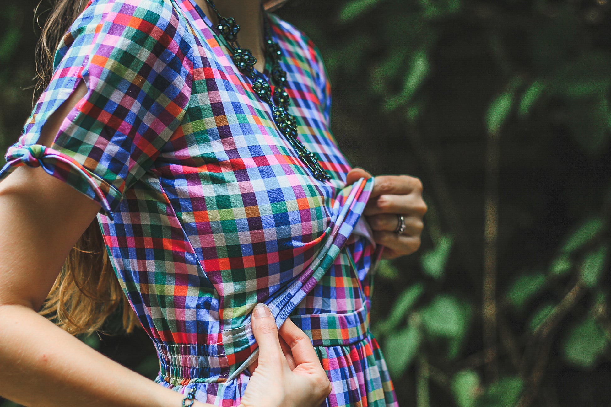 Woman wearing a colorful checkered modest nursing dress with a blurred green background