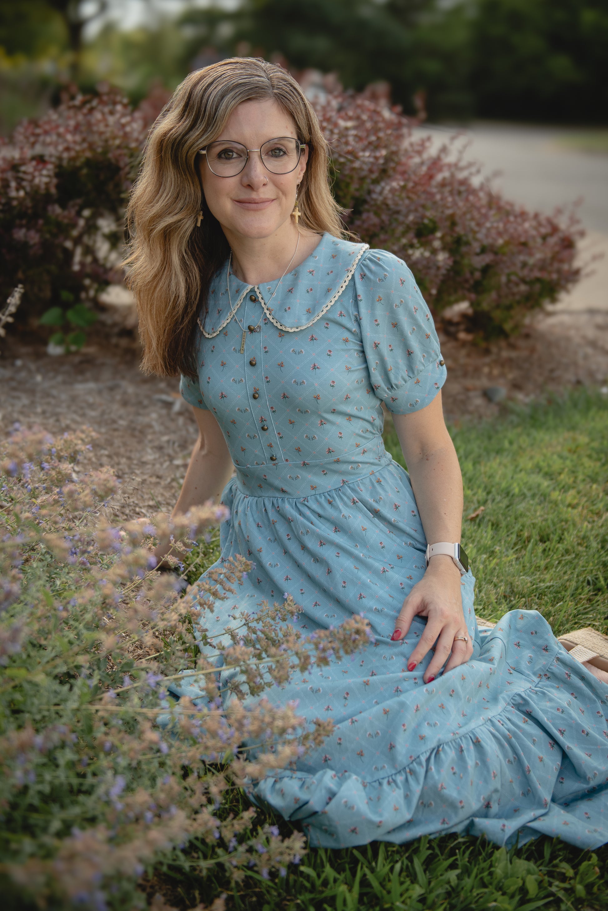 Woman in a blue modest nursing dress sitting among flowers outdoors
