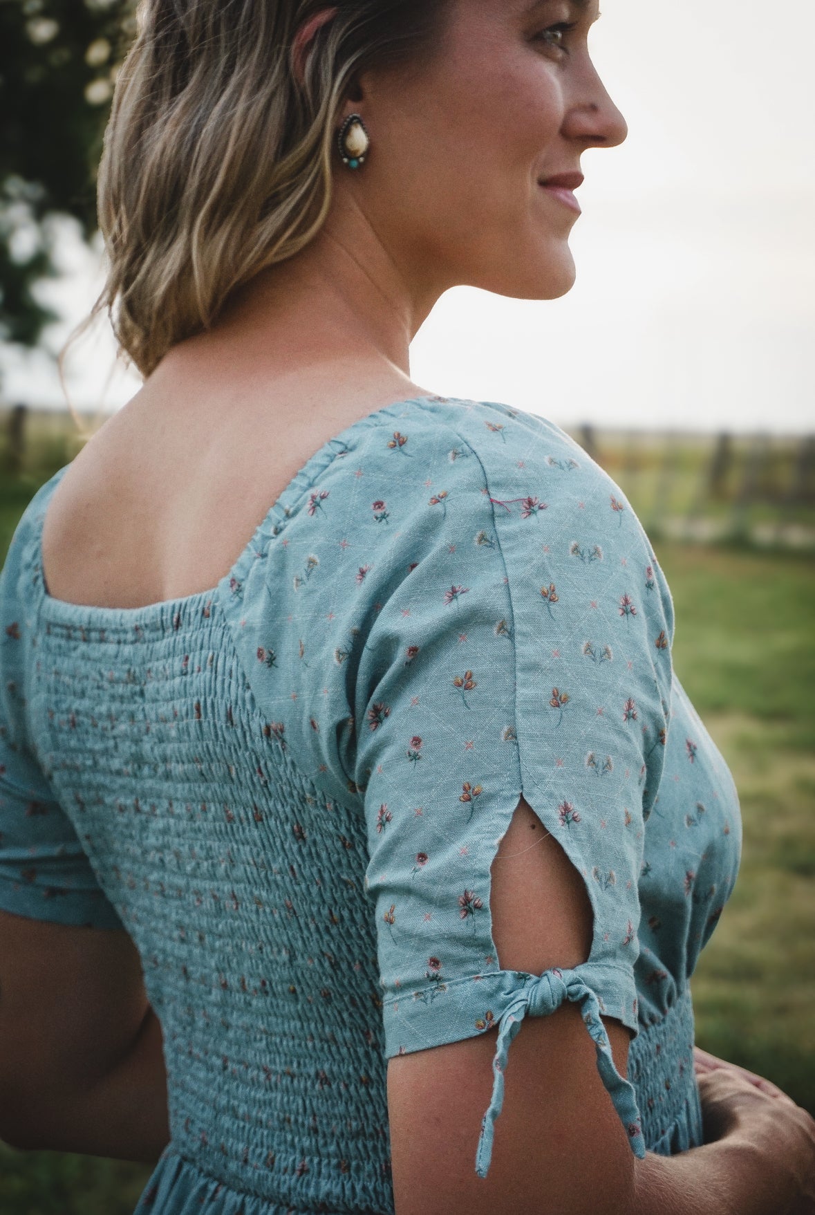 Woman wearing a blue floral modest nursing dress standing outdoors with a blurred background