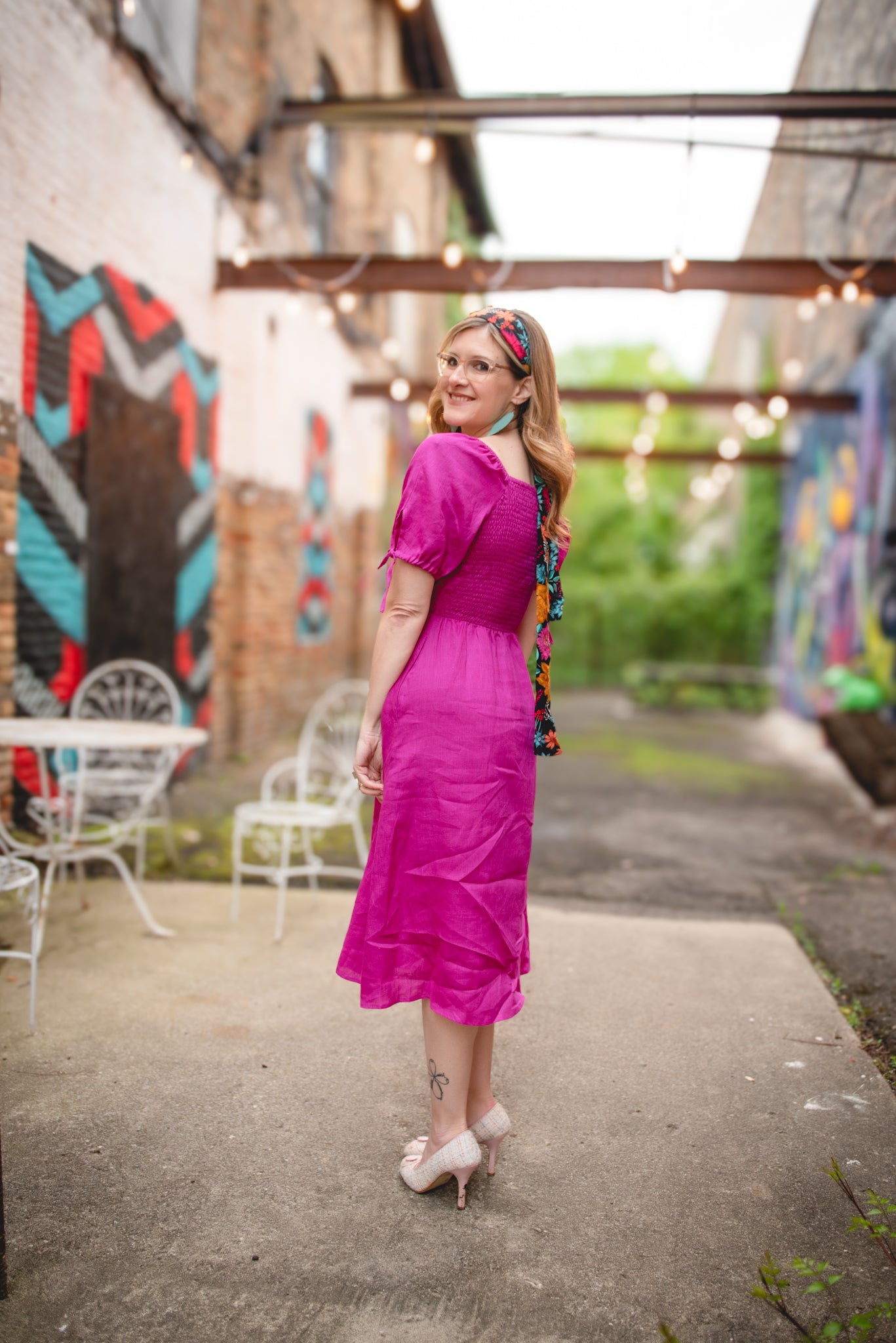 Woman in a pink modest nursing dress standing in an outdoor setting with colorful murals.