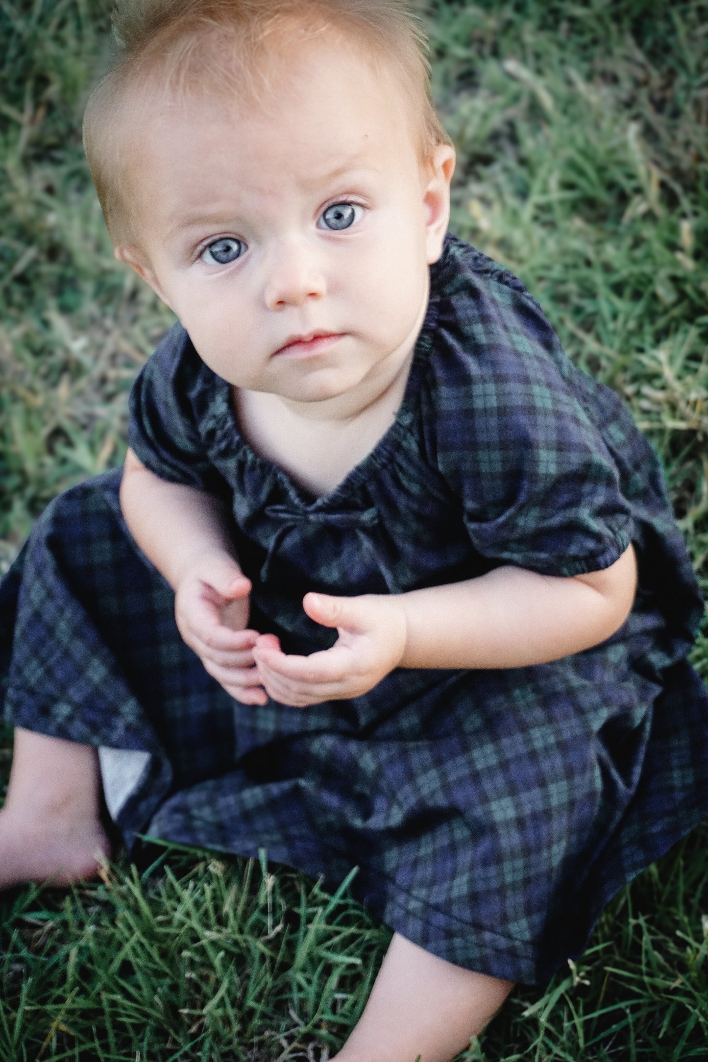 Baby in modest plaid dress sitting outdoors