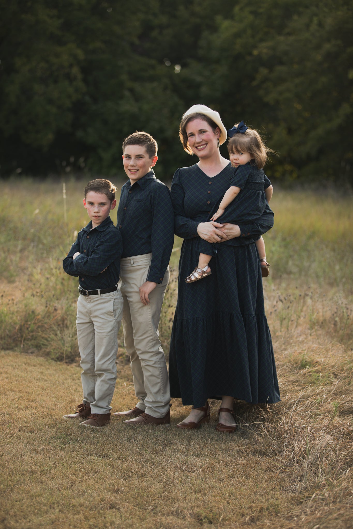 Woman in modest nursing dress holding child with two boys outdoors