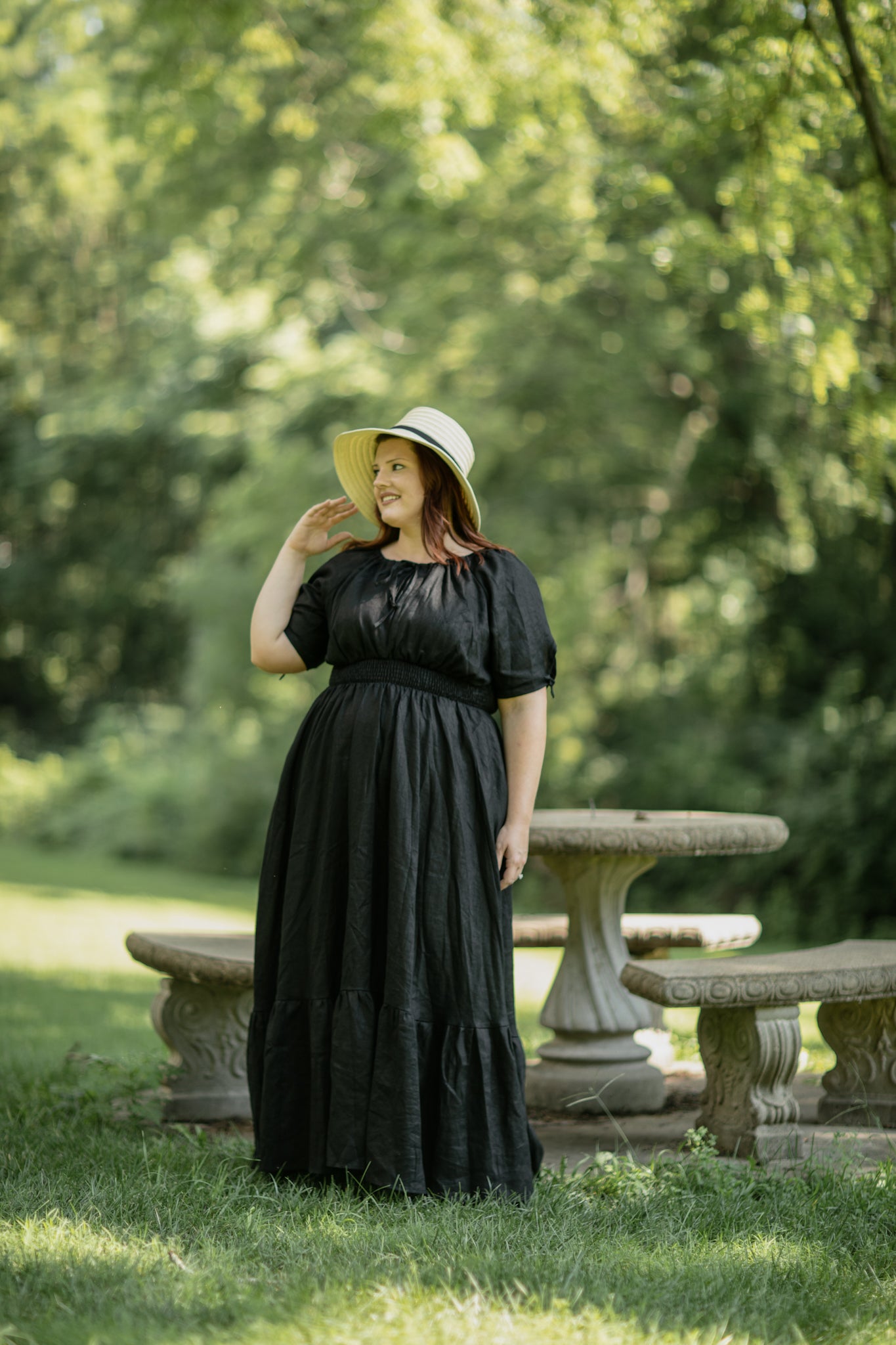 Woman in a black modest nursing dress standing outdoors with greenery in the background