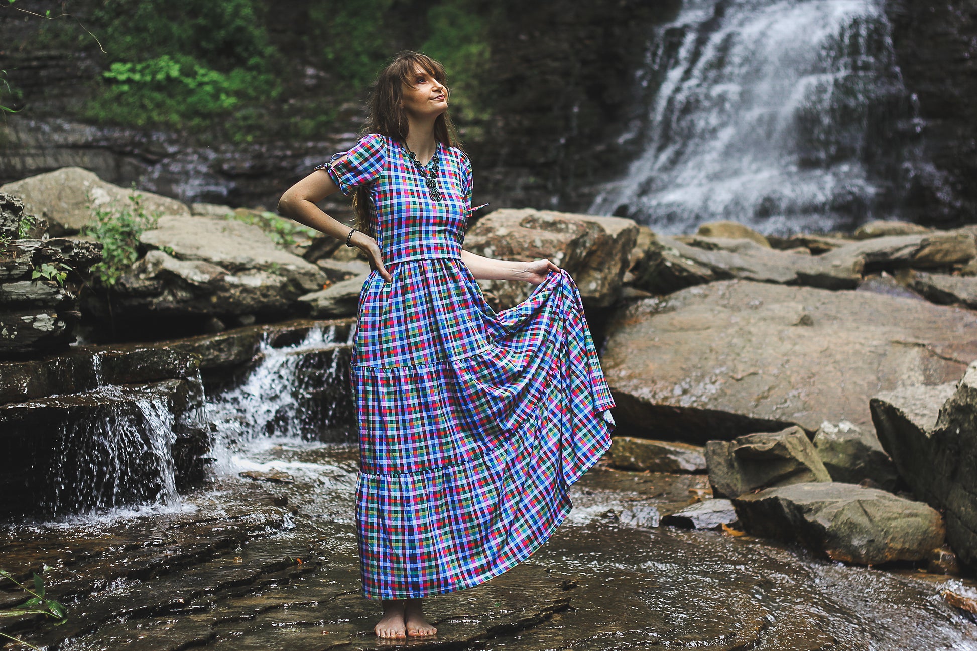 Woman in a plaid modest nursing dress standing by a waterfall