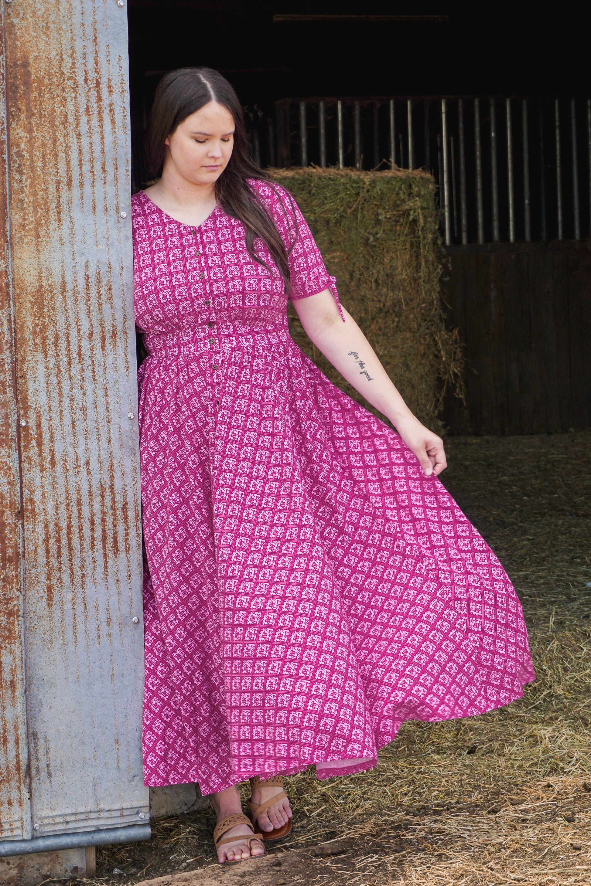 Woman wearing a pink modest nursing dress with a pattern, standing in an outdoor setting.