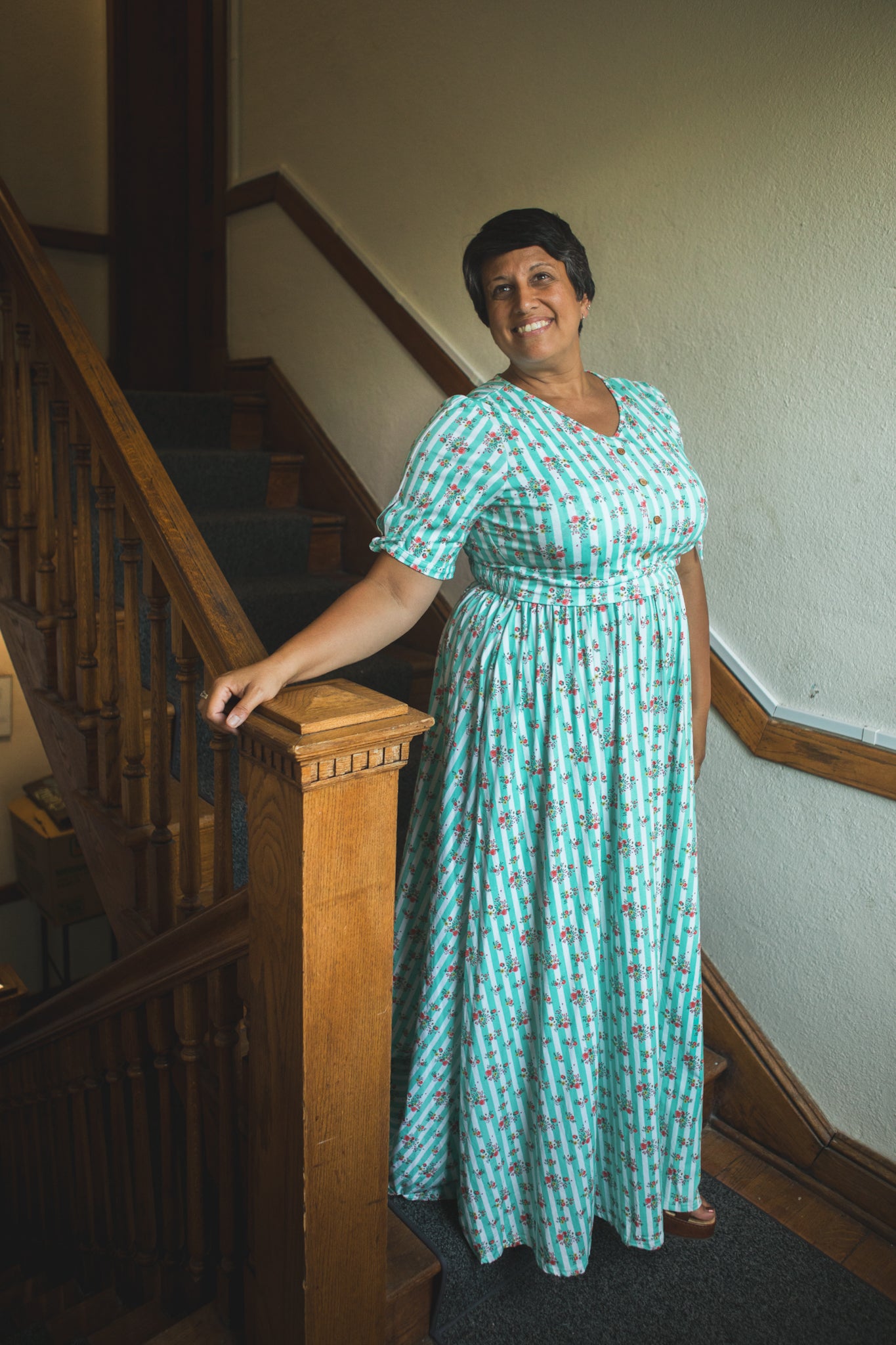 Woman in a green modest dress standing on a staircase.