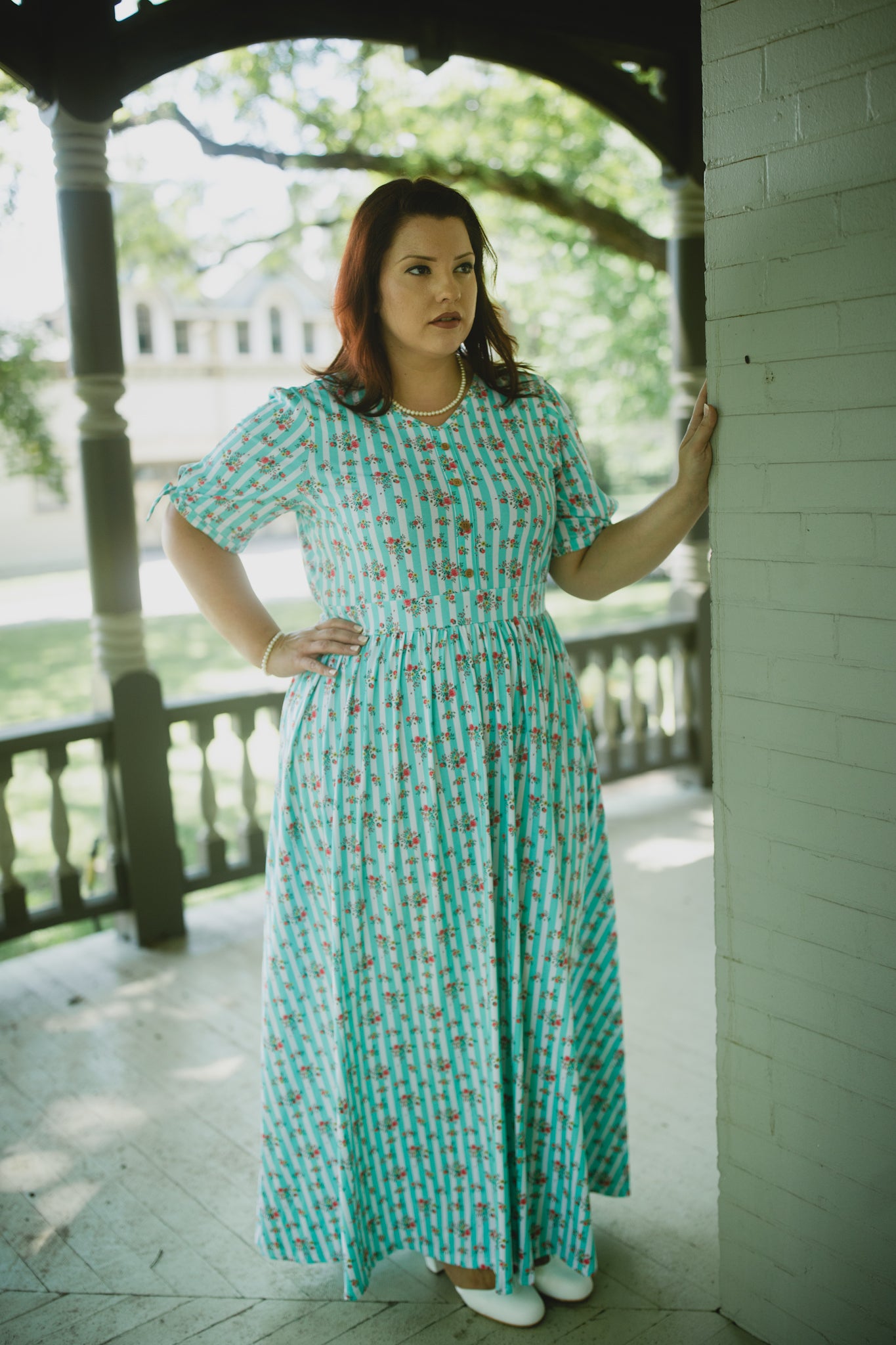 Woman in a green patterned modest nursing dress standing on a porch
