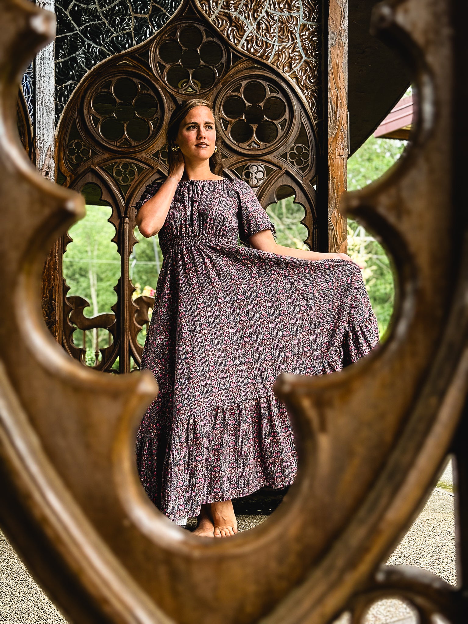 Woman in a long modest nursing dress standing behind ornate wooden gates.