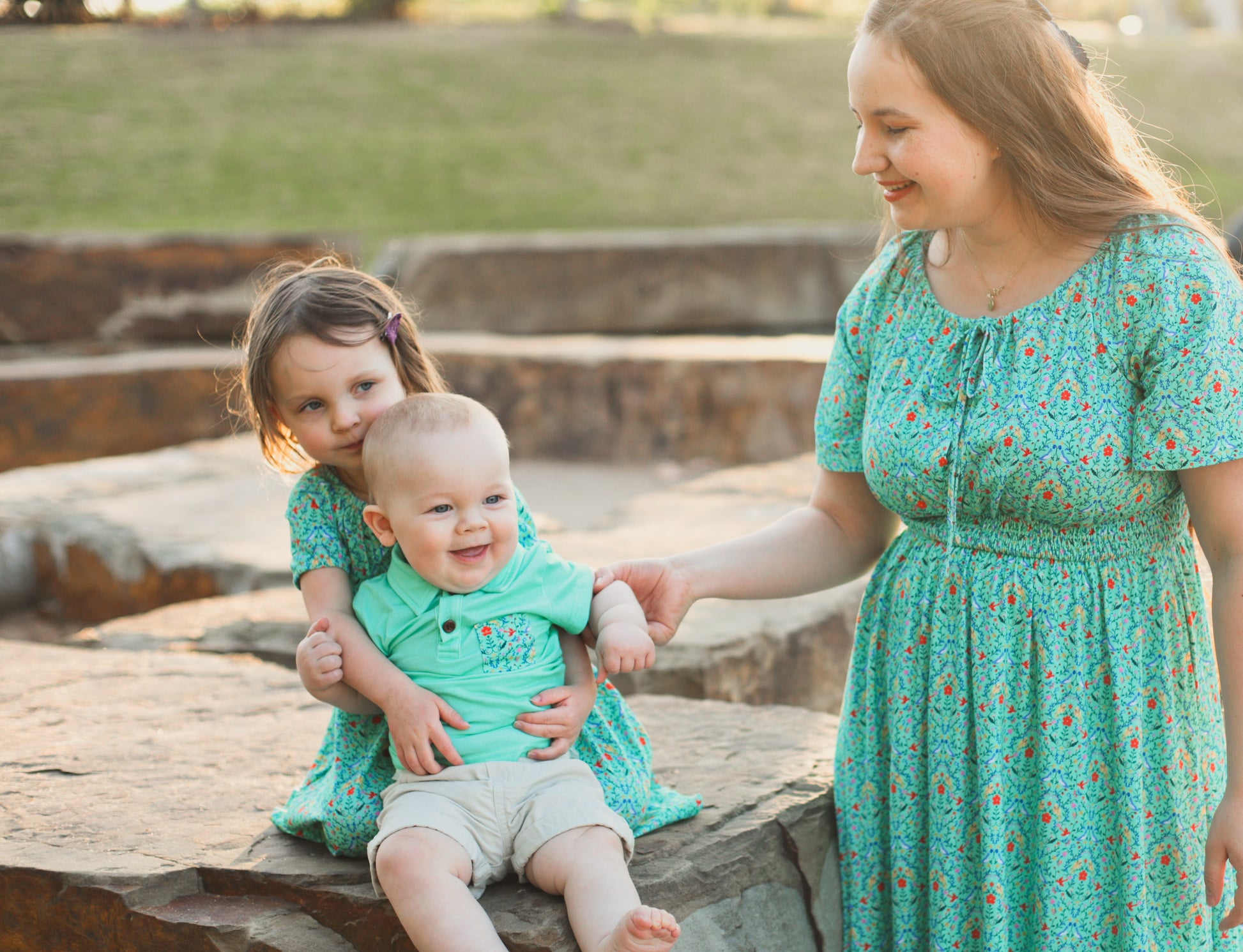 Young girl wearing a modest green dress with her mother in a modest green nursing dress with baby son in hand