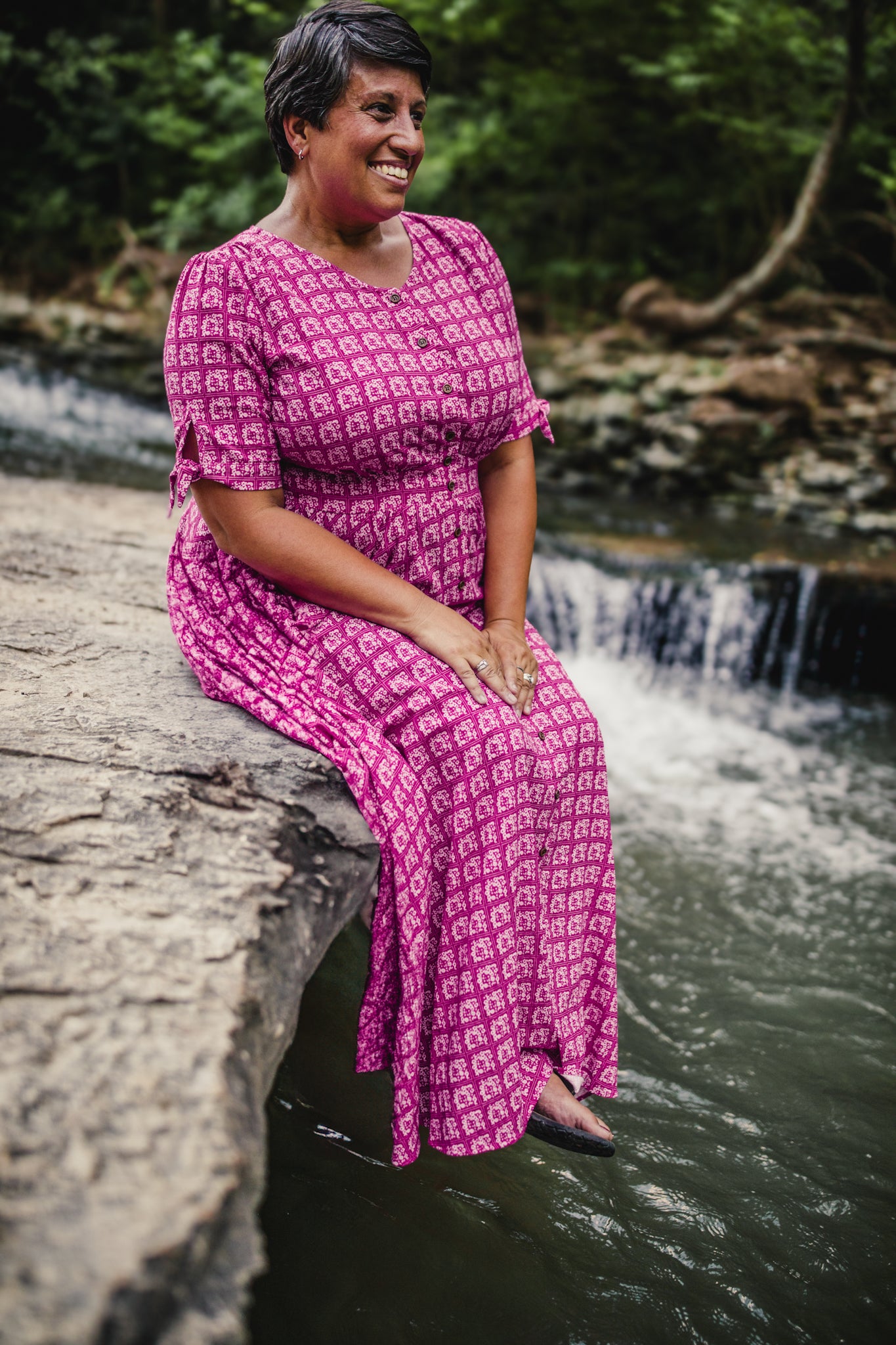 Woman in a pink modest nursing dress sitting on a rock by a stream