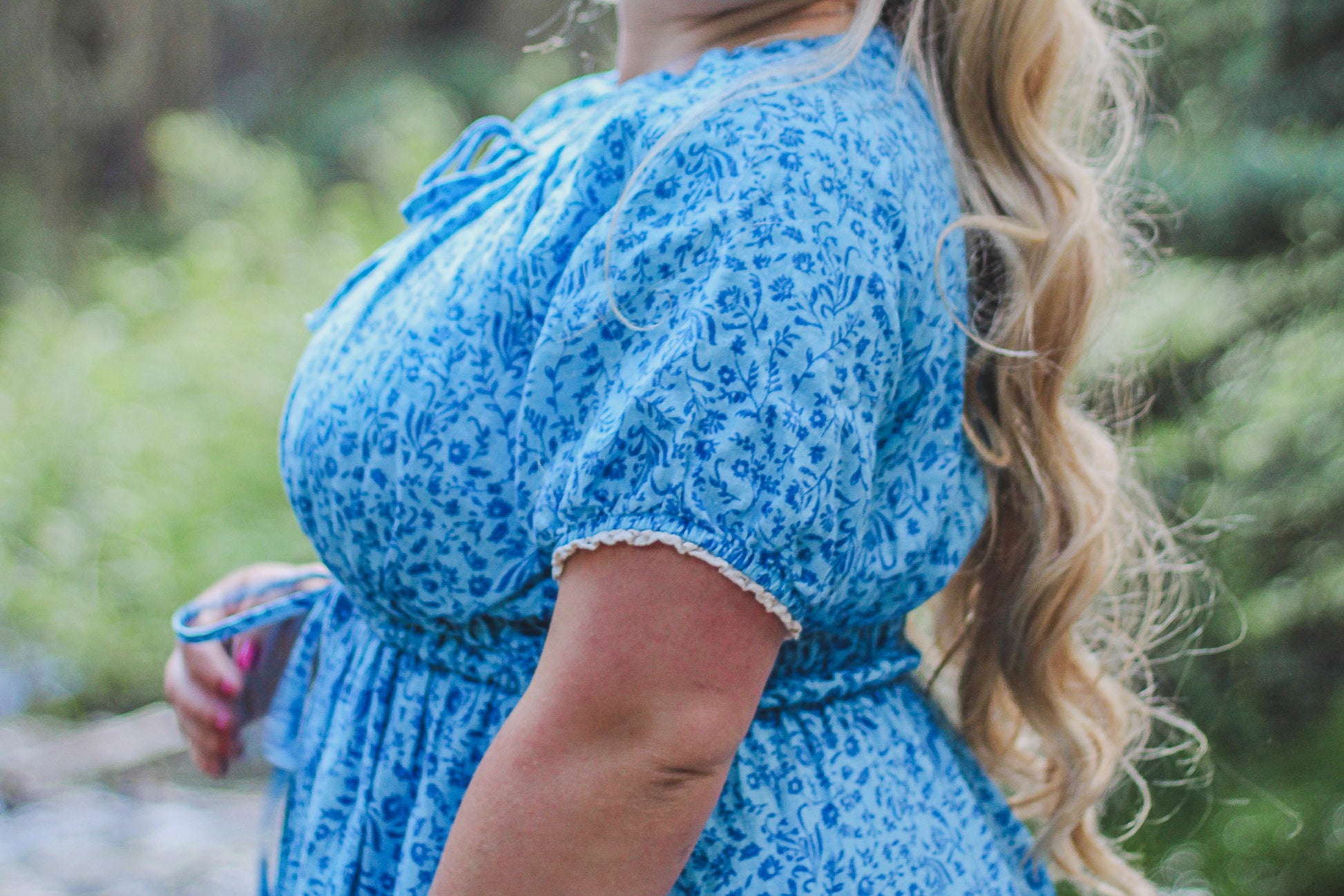 Person wearing a blue floral modest nursing dress with a blurred natural background