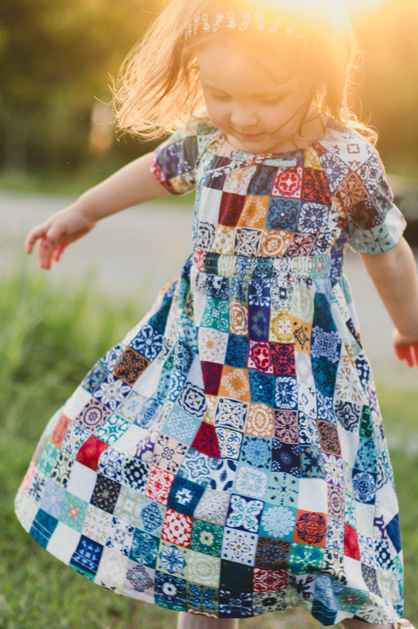 Child wearing a colorful patchwork dress outdoors with a blurred background