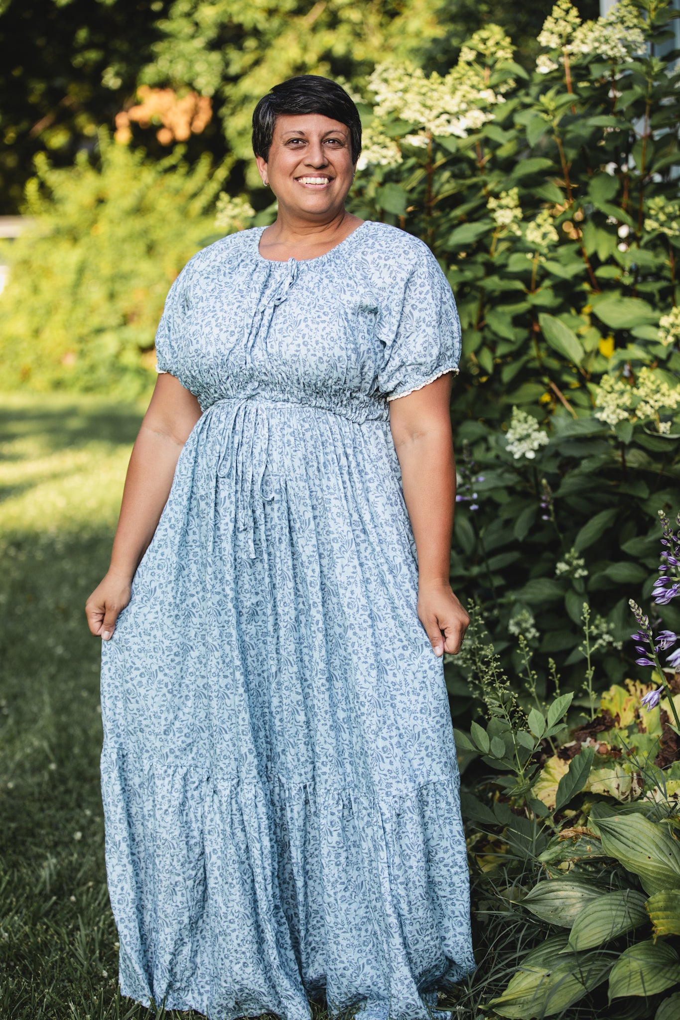 Woman wearing a modest blue nursing dress standing in a garden