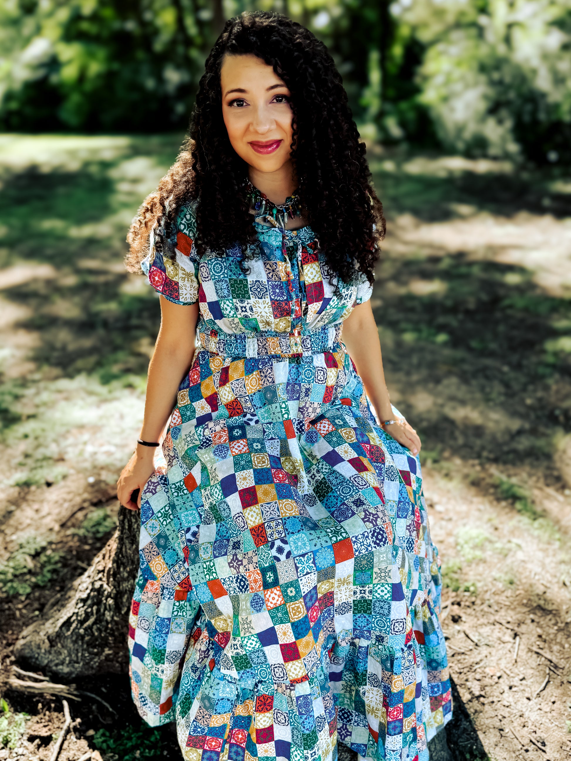 Woman wearing a colorful patchwork modest nursing dress sitting outdoors on a log.