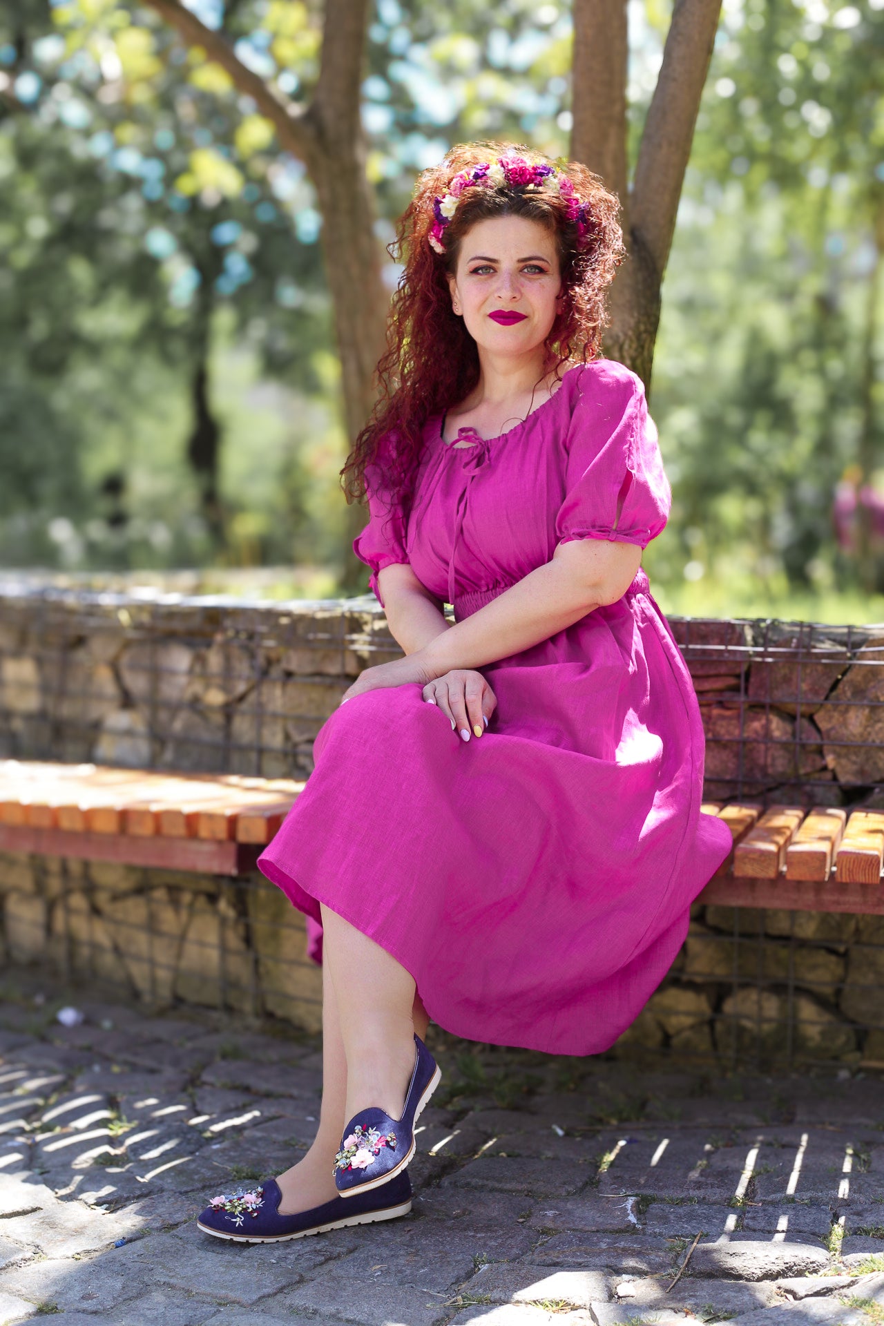 Woman in a pink modest nursing dress sitting on a bench outdoors with trees in the background