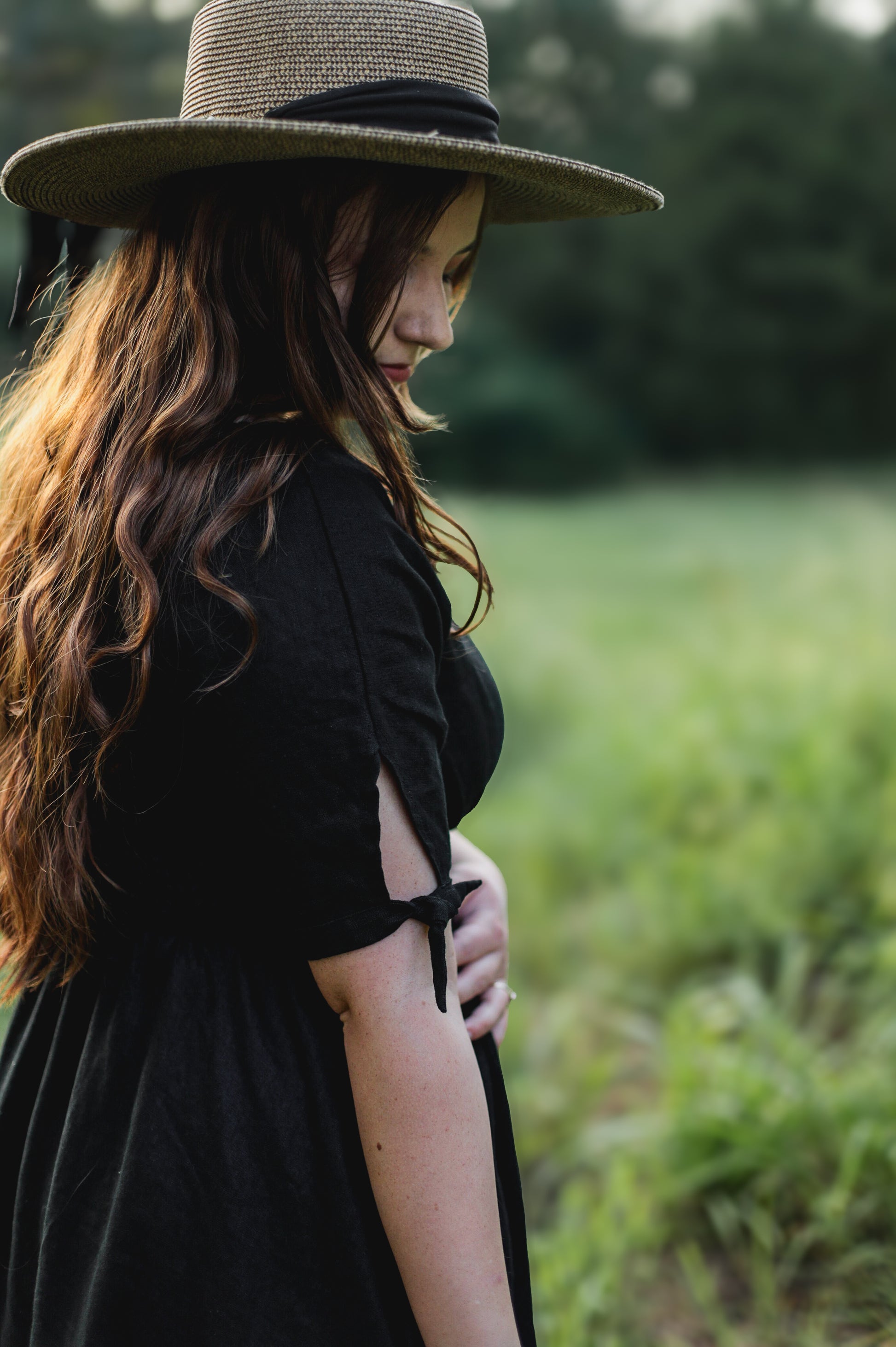Woman in a black modest nursing dress and wide-brimmed hat standing in a field
