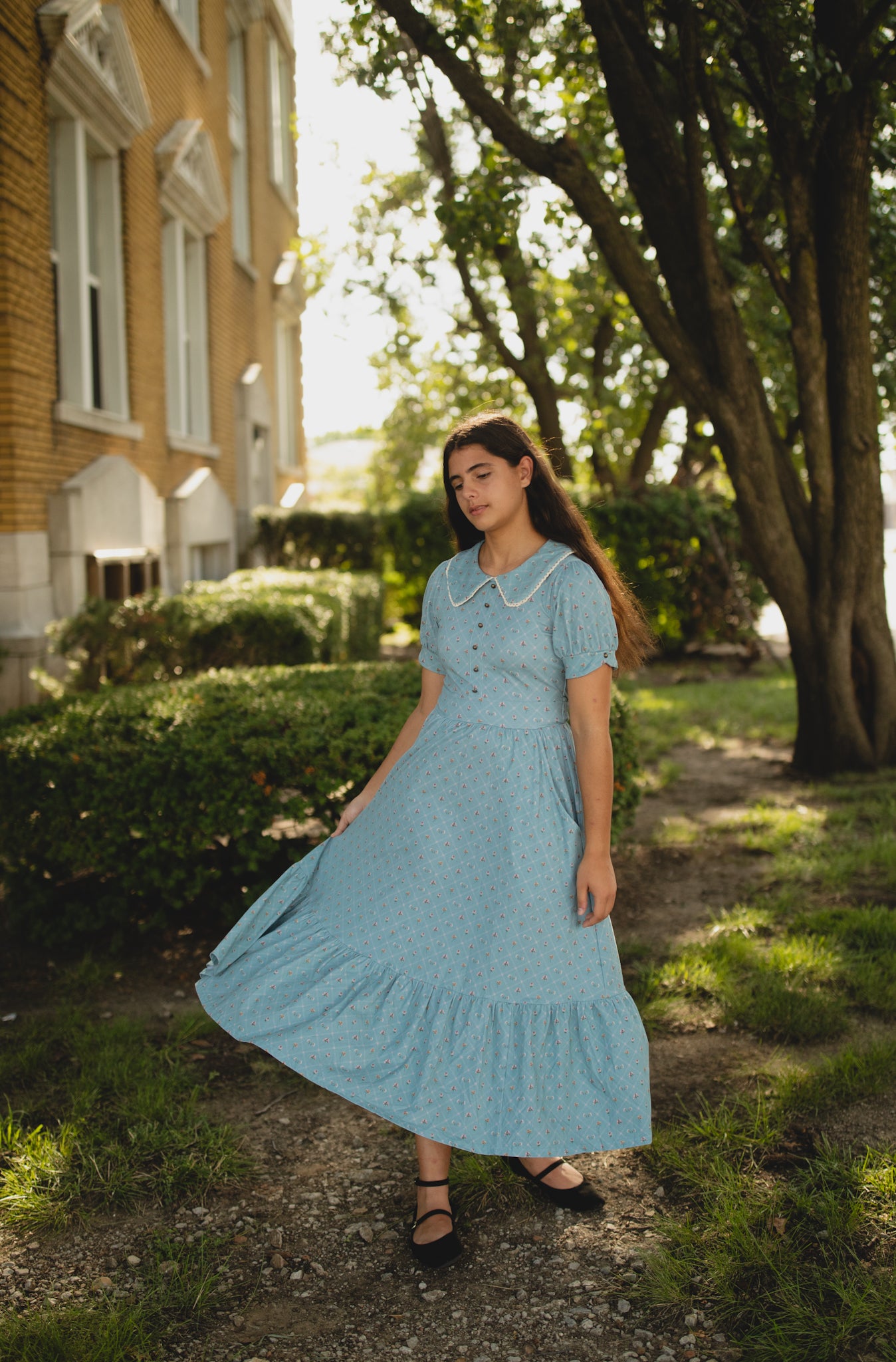 Woman in a blue dress standing outdoors near a building with trees