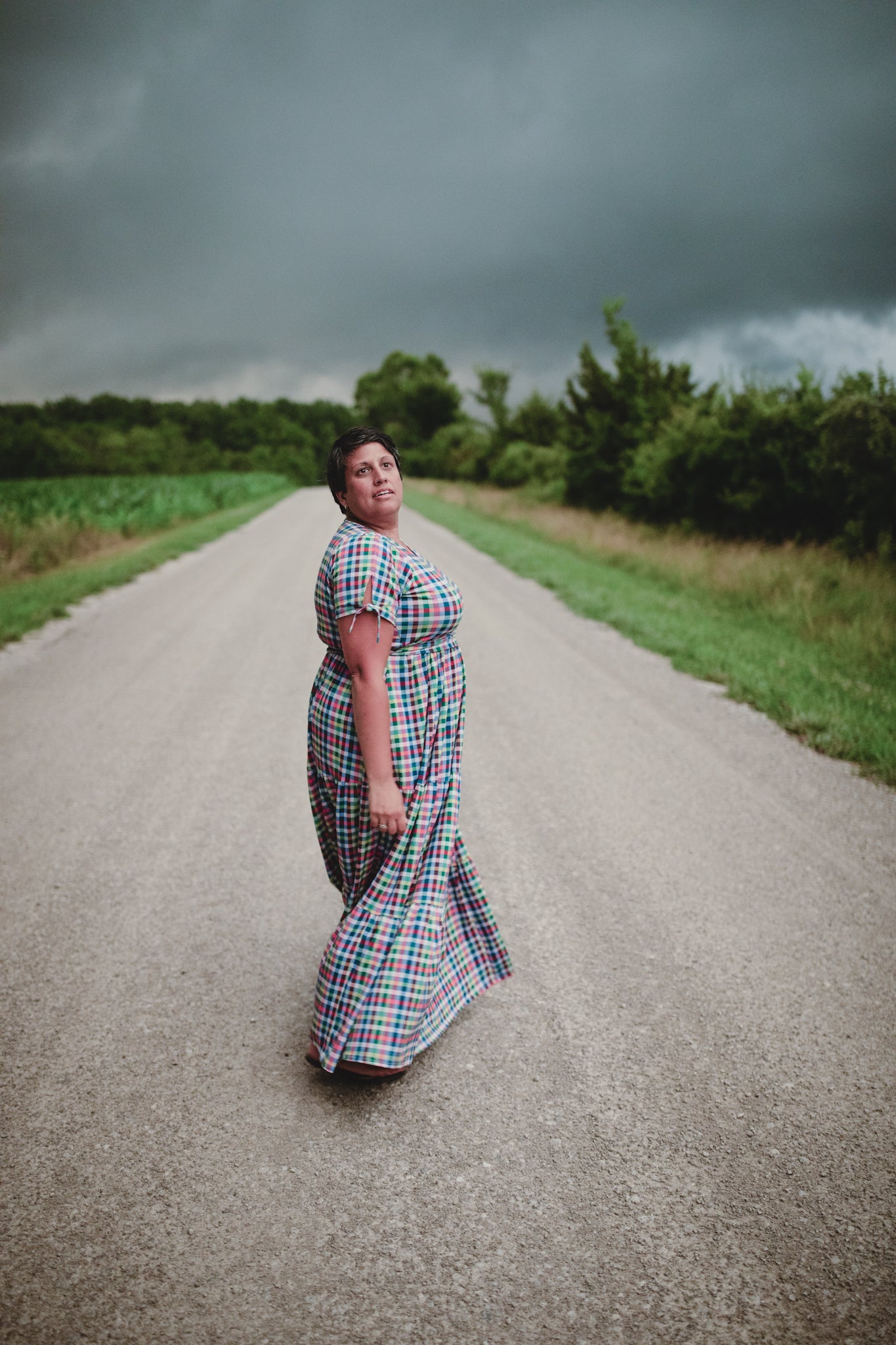 Woman in a plaid modest nursing dress standing on a rural road with stormy skies.