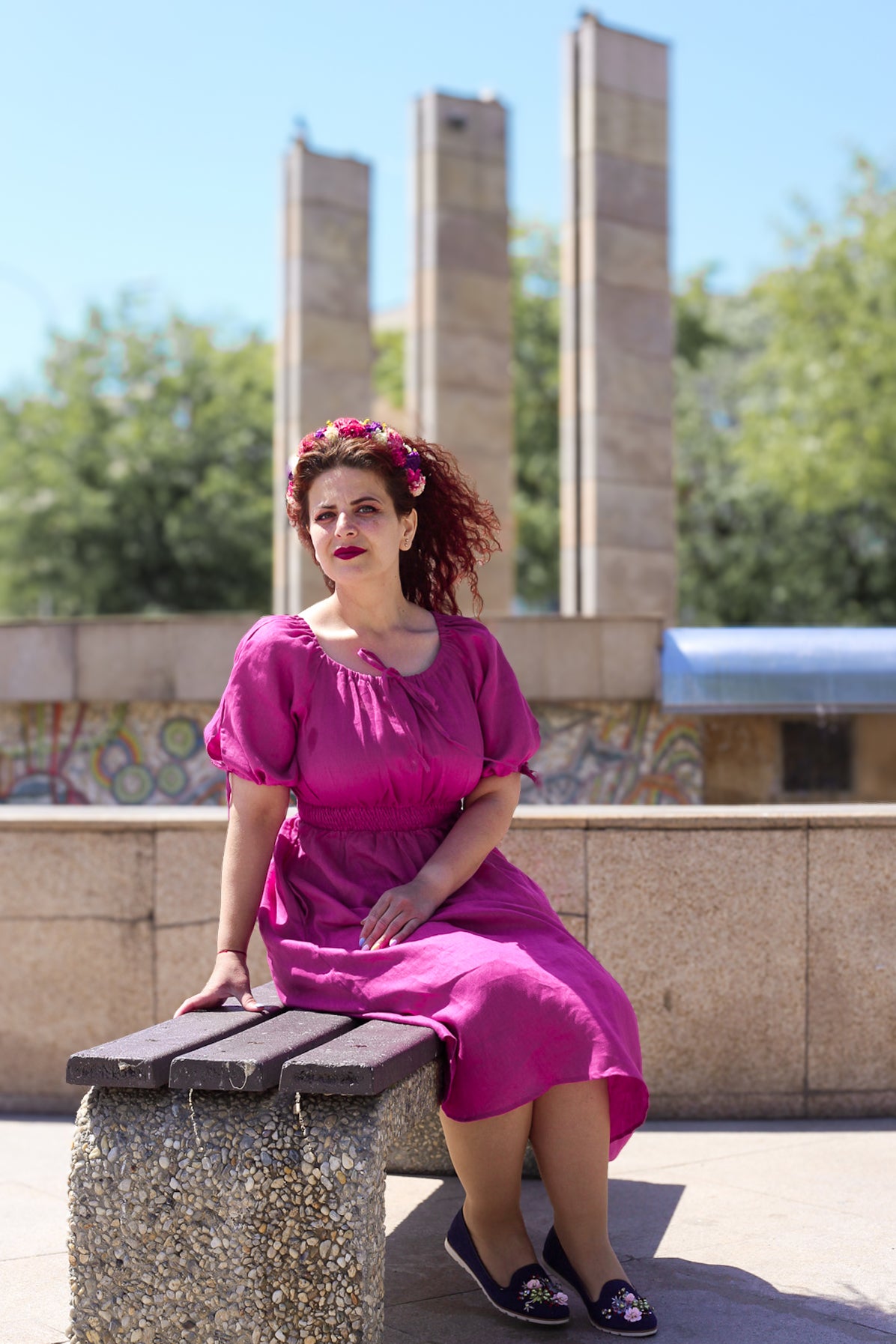 Woman in a pink modest nursing dress sitting on a bench with a scenic background