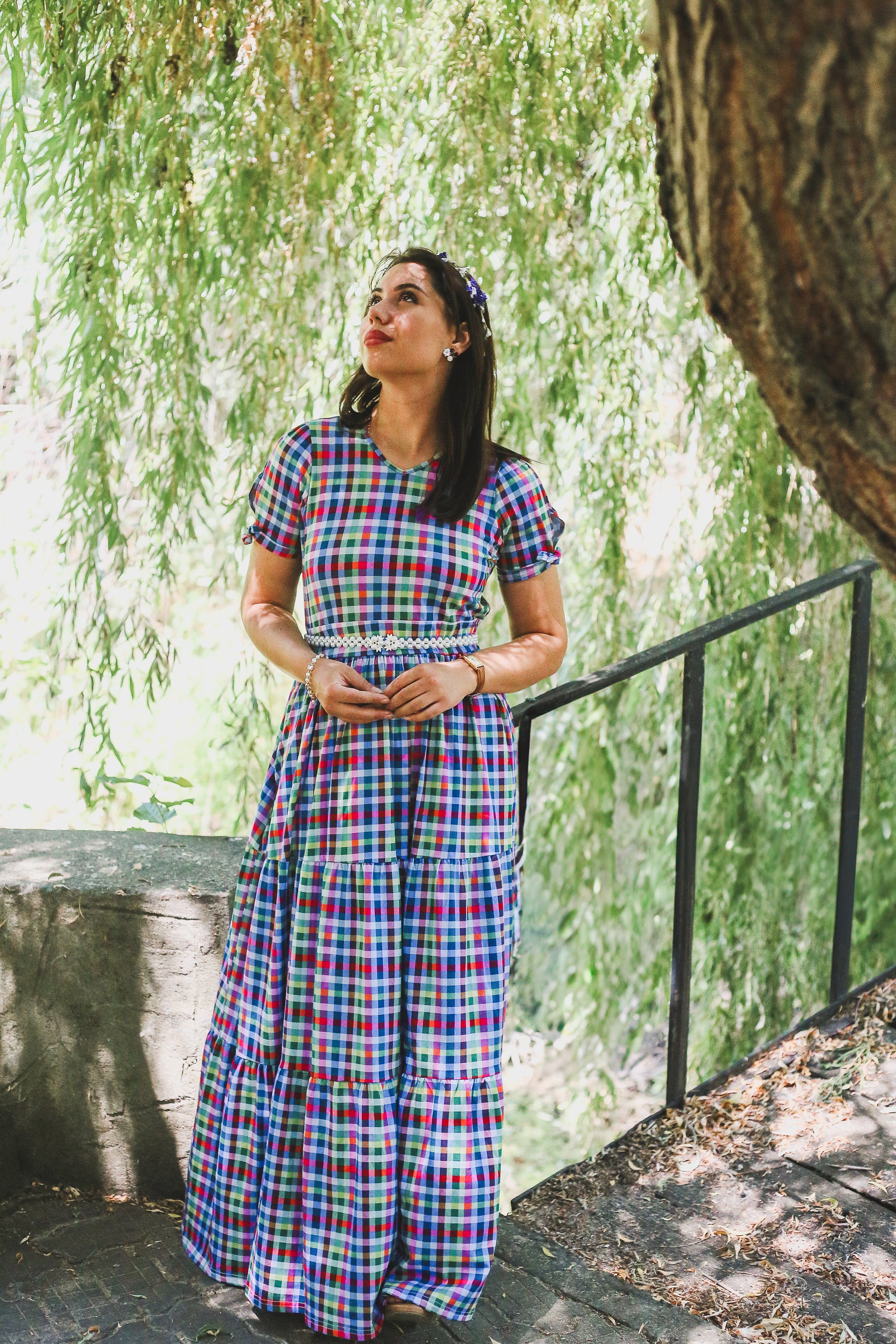 Woman in a plaid modest nursing dress standing in front of a tree with greenery