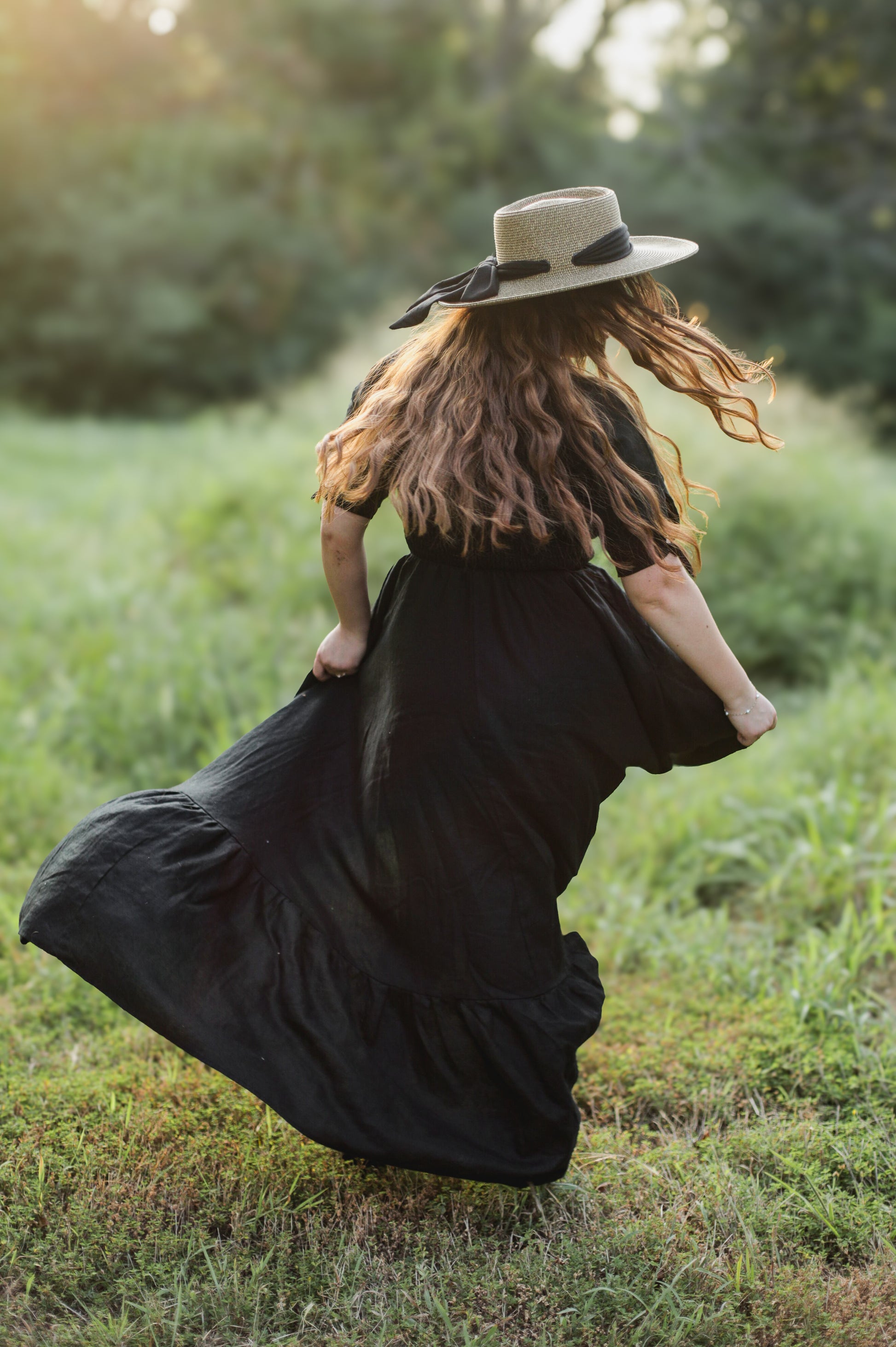 Woman in a black modest nursing dress and hat running through a grassy field